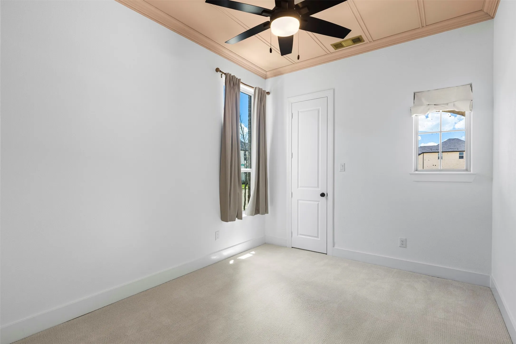 Carpeted flooring, paneled door, coffered ceiling, ceiling fan with integrated lighting, and multiple windows
