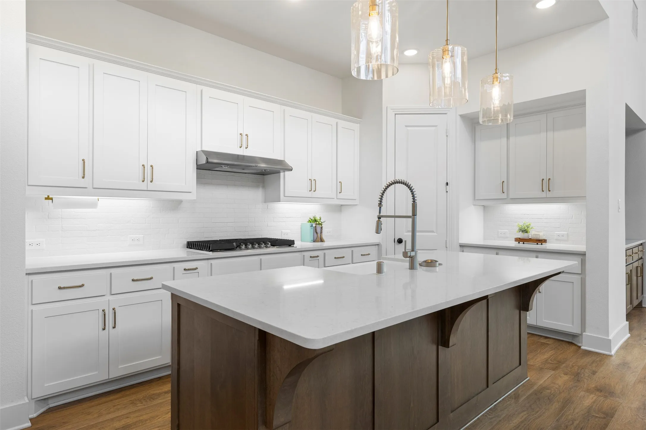 Kitchen featuring a large center island with a light-toned countertop, white cabinetry with gold-toned hardware, a subway tile backsplash, and wood-finish flooring