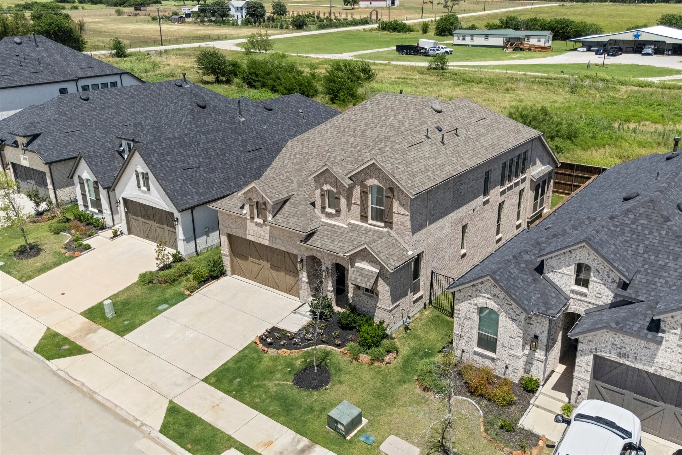Brick exterior with decorative dormer windows, attached garage, concrete driveway, and manicured landscaping