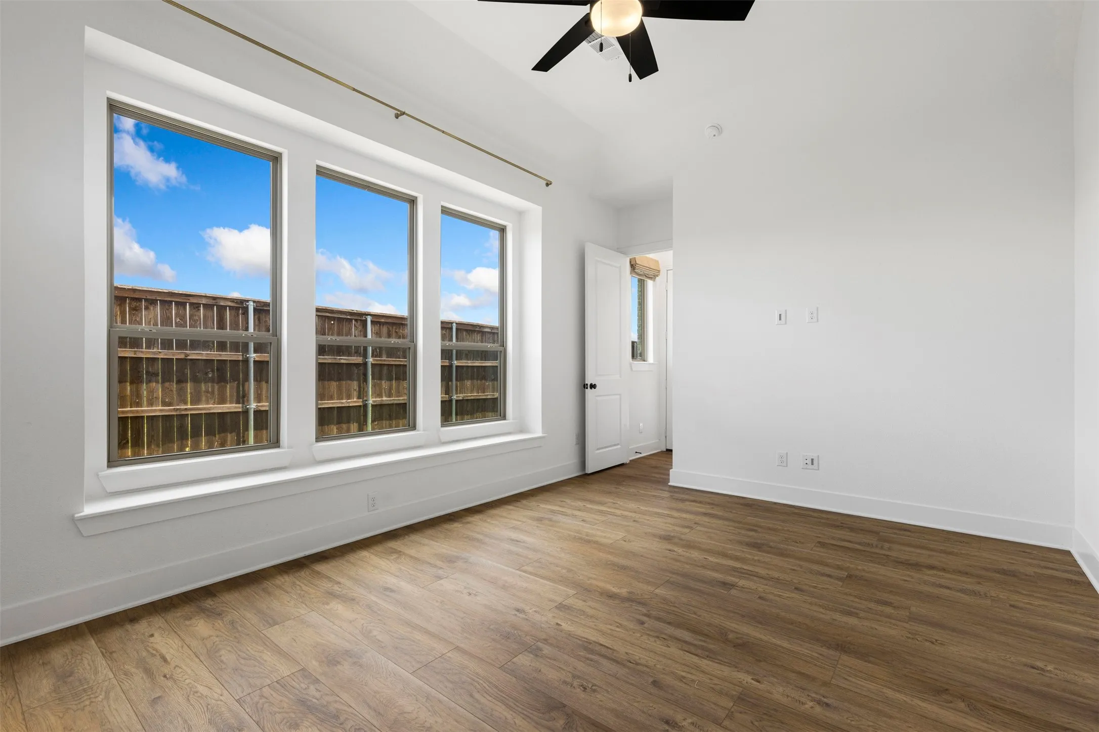 Expansive room featuring wood-finish flooring, a contemporary ceiling fan, and a wall of three large windows