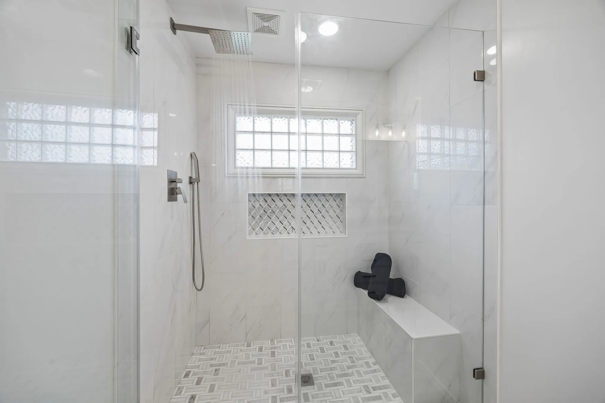Glass-enclosed shower with a rainfall showerhead, integrated bench, recessed shelving with decorative tile, and a glass block window