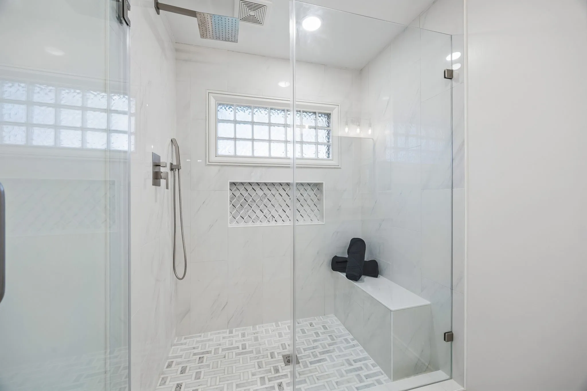Glass-enclosed shower with a rainfall showerhead, handheld shower fixture, built-in bench, and tiled niche