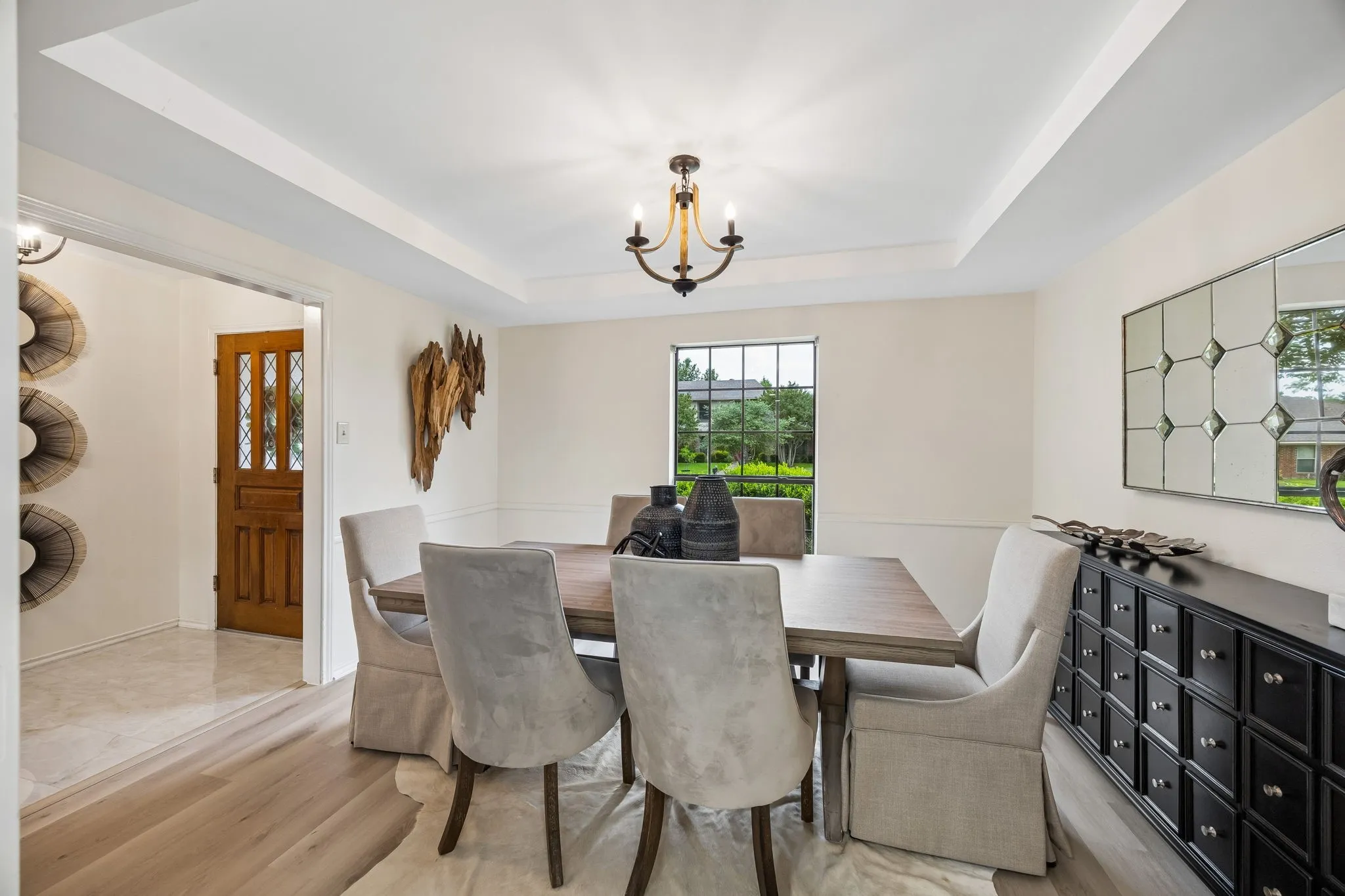Tray ceiling with a chandelier, wood-finish flooring, white wall paneling, and a large window