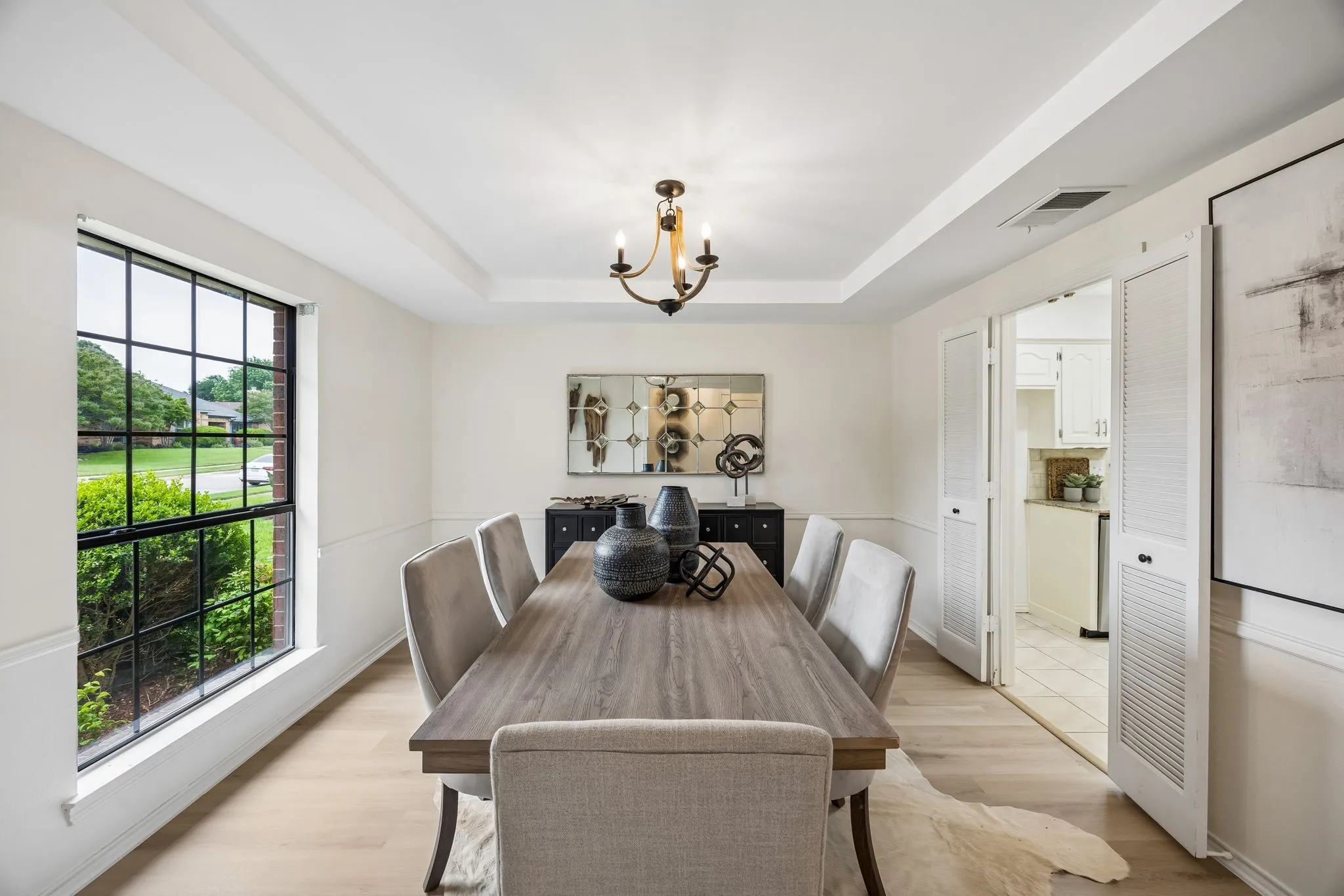 Tray ceiling, wood-finish flooring, wainscoting, black grid window, and a built-in chandelier