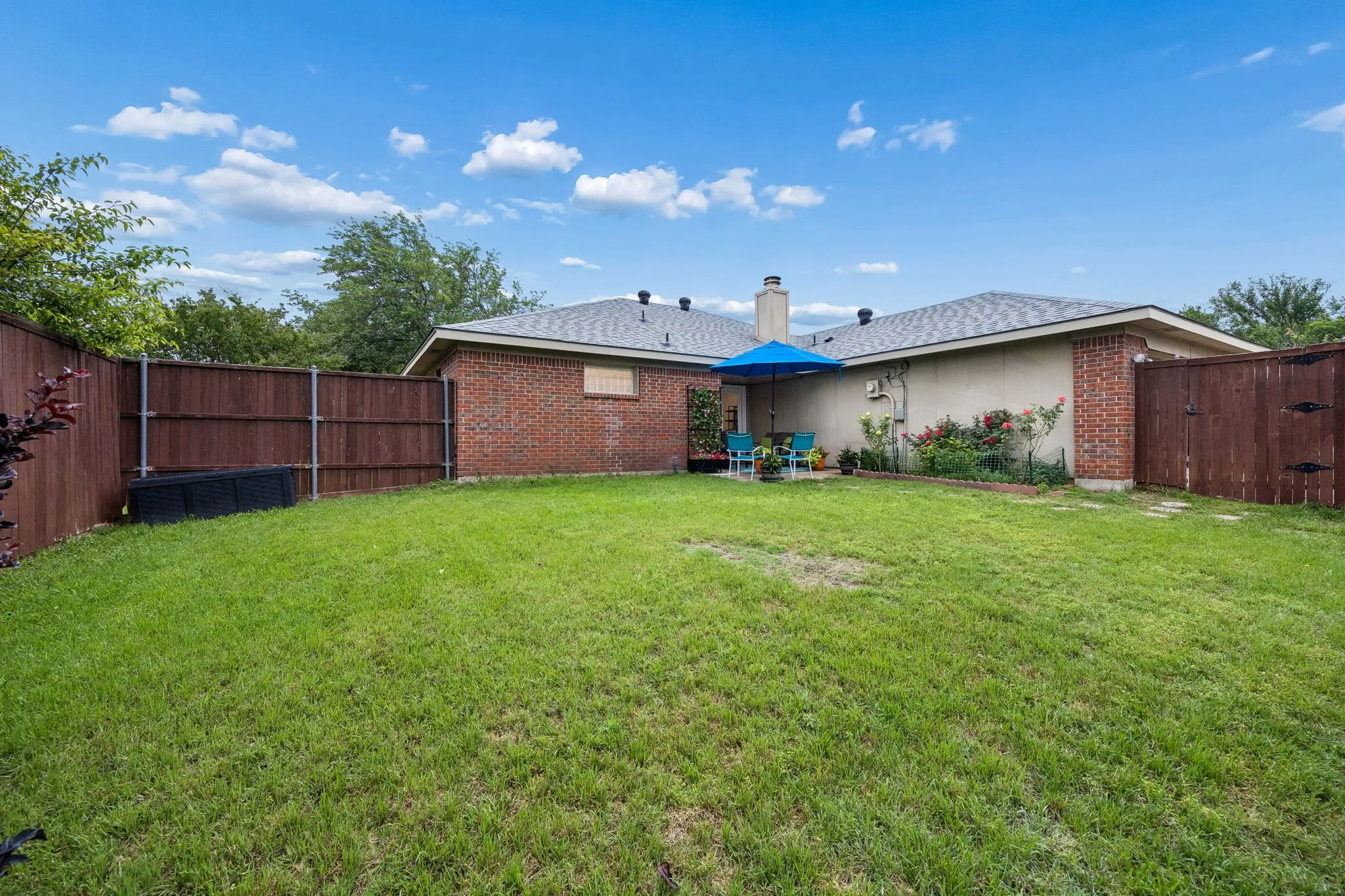 Expansive backyard featuring a lush lawn, solid wood fencing, and a brick exterior