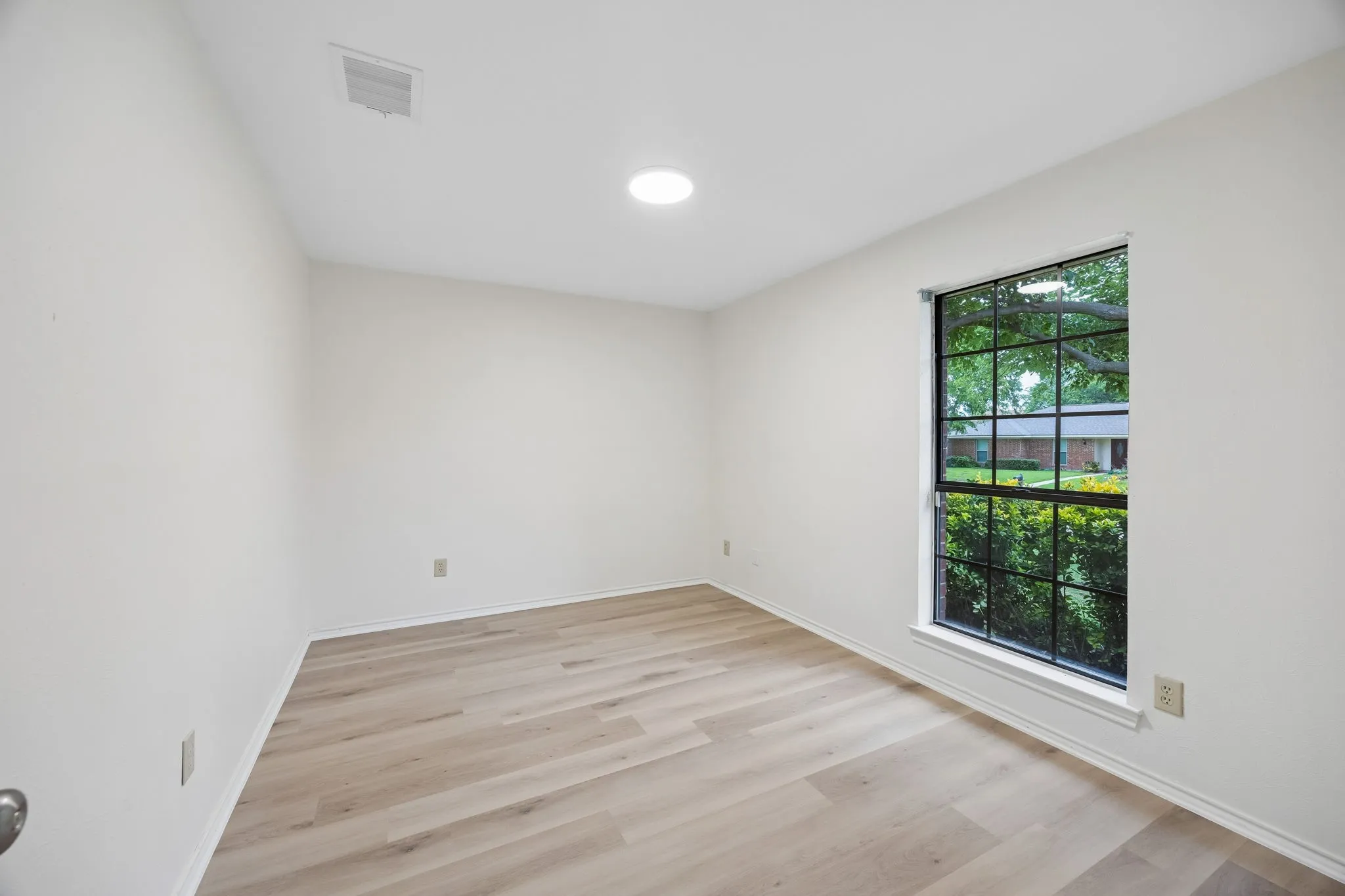 Neutral wall finishes, recessed ceiling lighting, wood-finish flooring, and a multi-pane window with exterior greenery