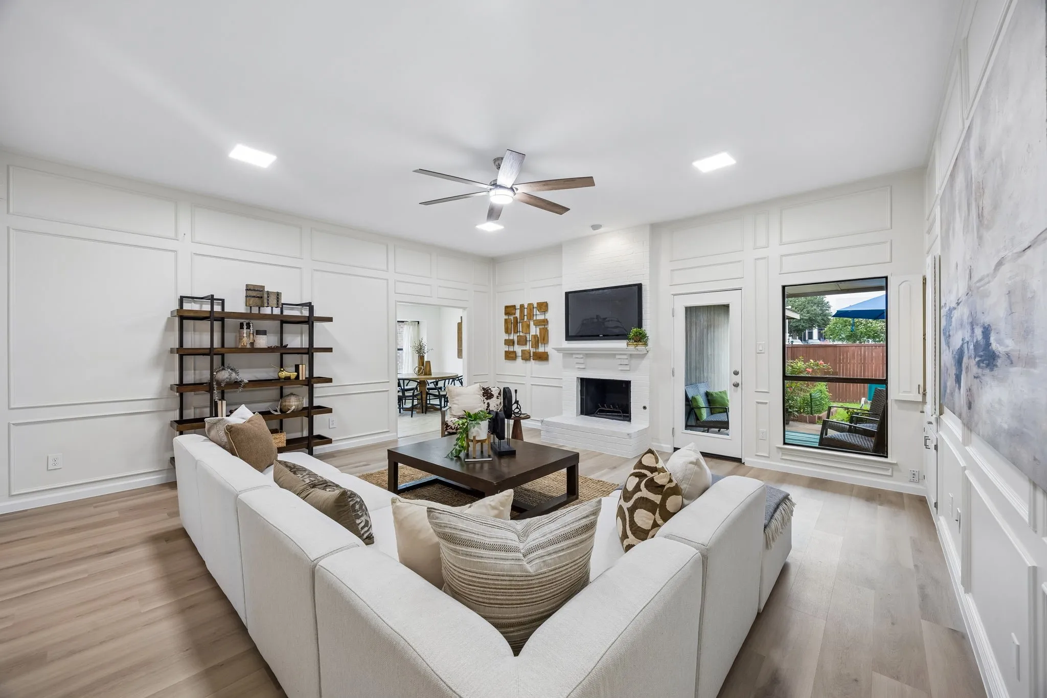 Living area featuring light wood-finish flooring, white paneling, and a ceiling fan