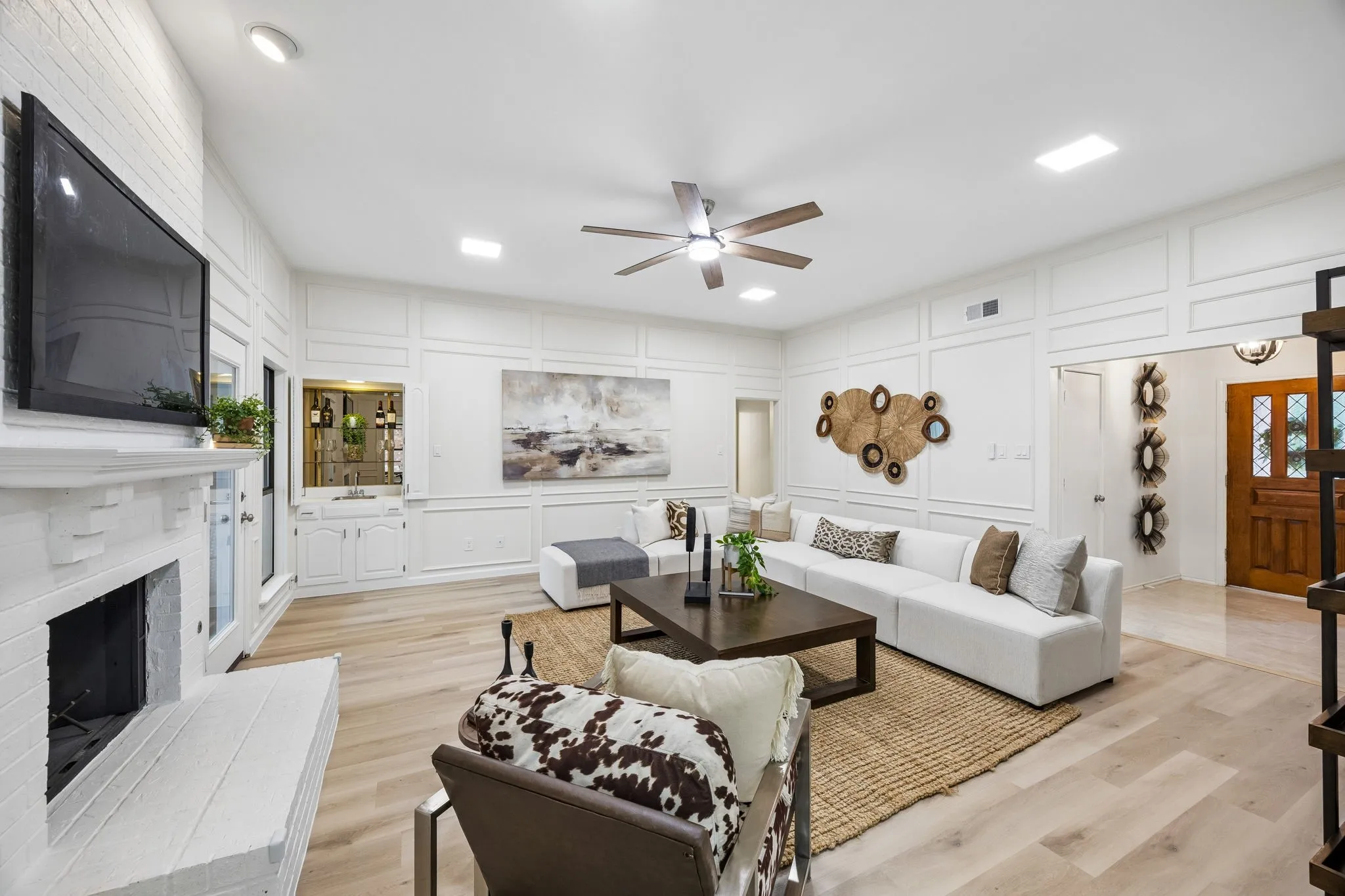 Spacious living area featuring light wood-finish flooring, a white brick fireplace, and built-in wet bar with cabinetry
