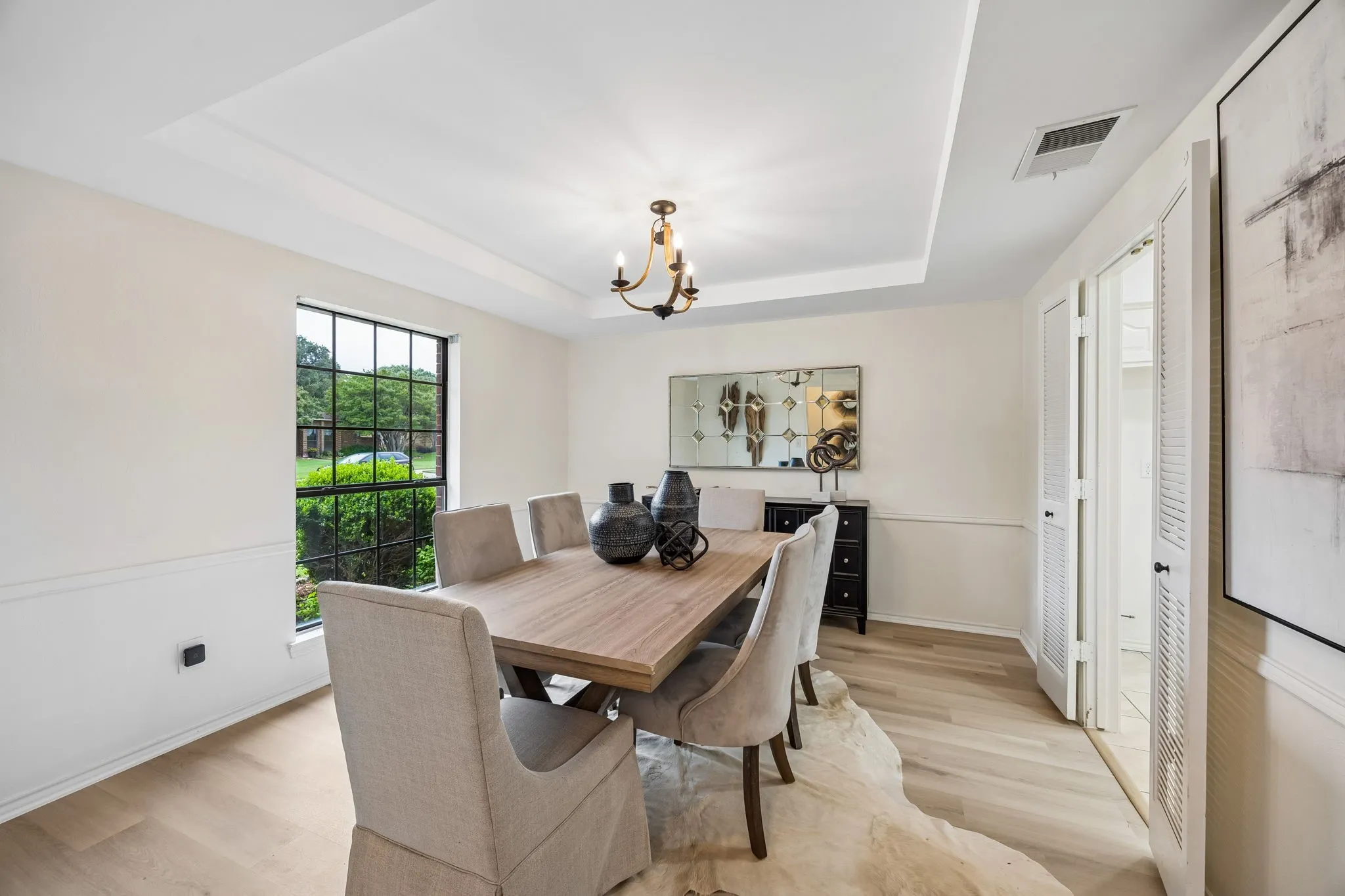 Tray ceiling with a bronze-finish chandelier, wood-finish flooring, and wainscoting
