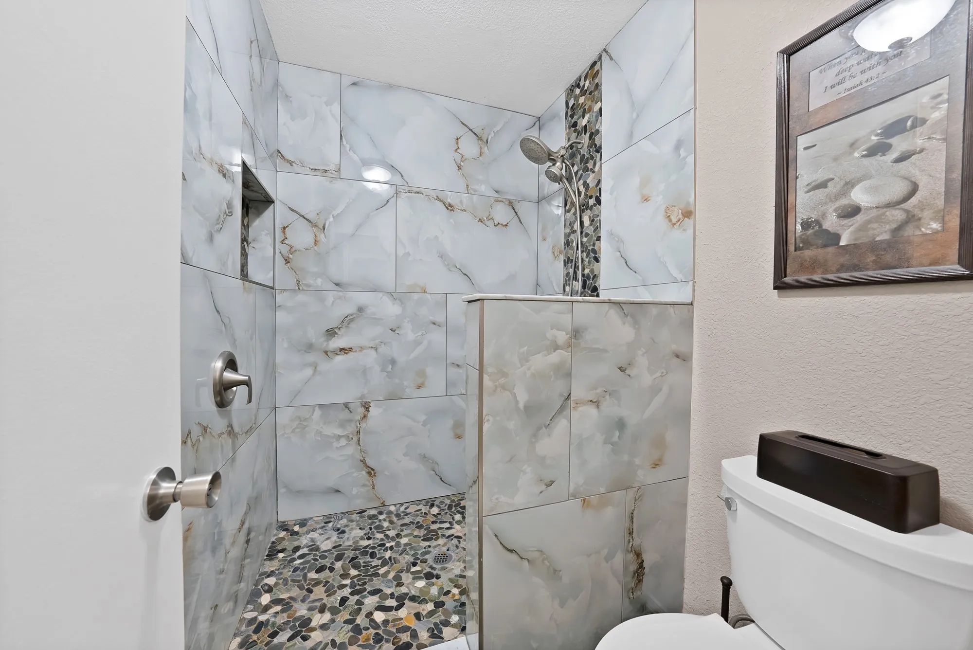 Walk-in shower featuring large format tiled walls, pebble shower floor, built-in shower niche, and brushed nickel fixtures