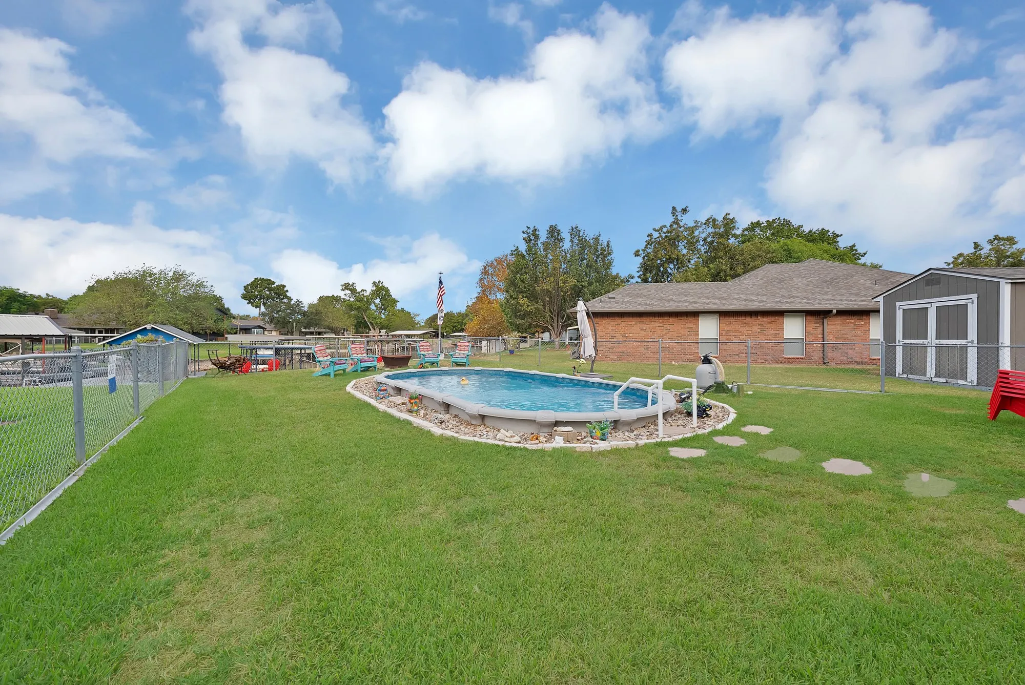 Expansive yard featuring a chain-link fence, an above-ground pool with stone edging, a stepping stone path, and a storage shed