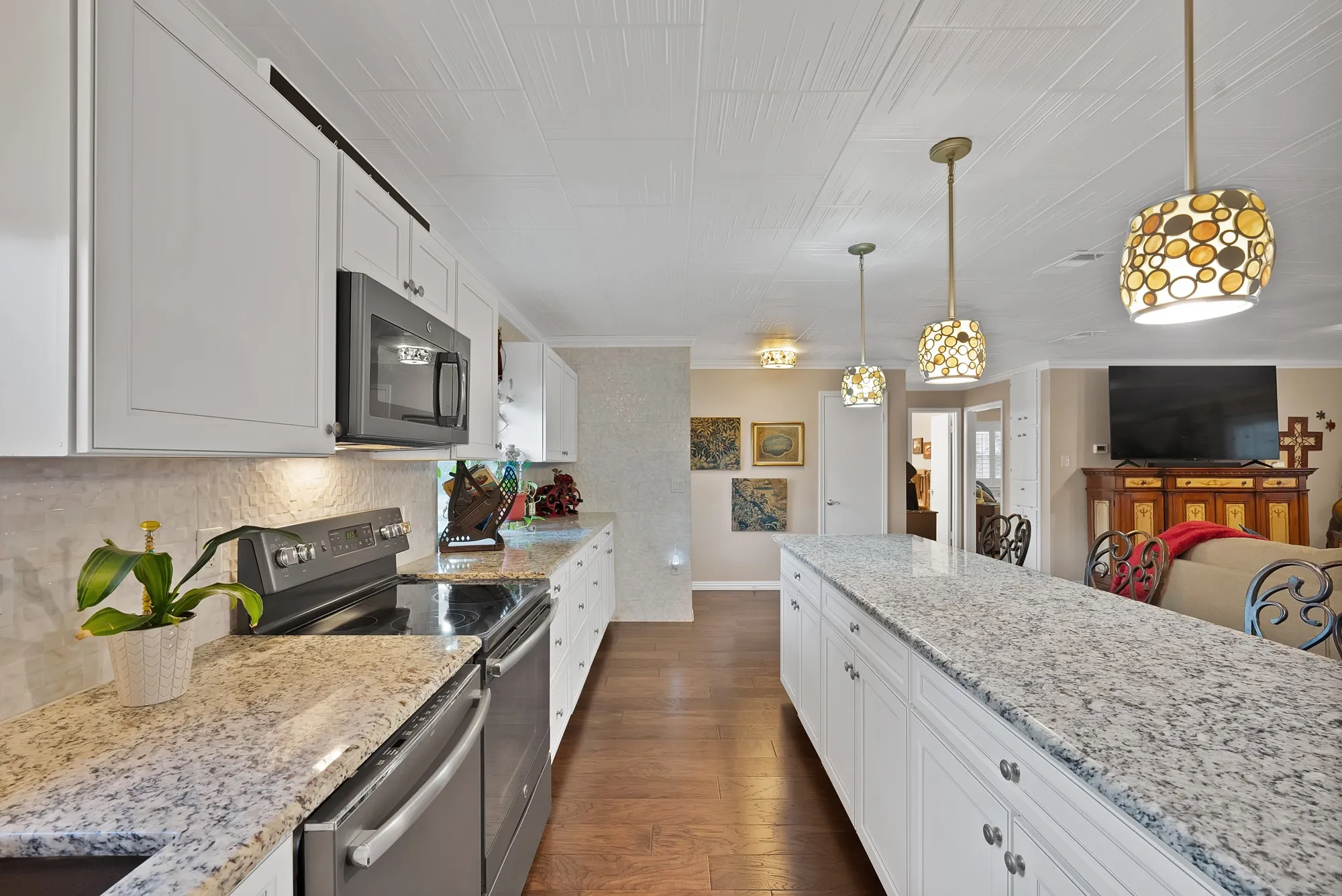 White shaker cabinetry, stainless steel appliances, speckled stone countertops, wood-finish flooring, and decorative pendant lighting