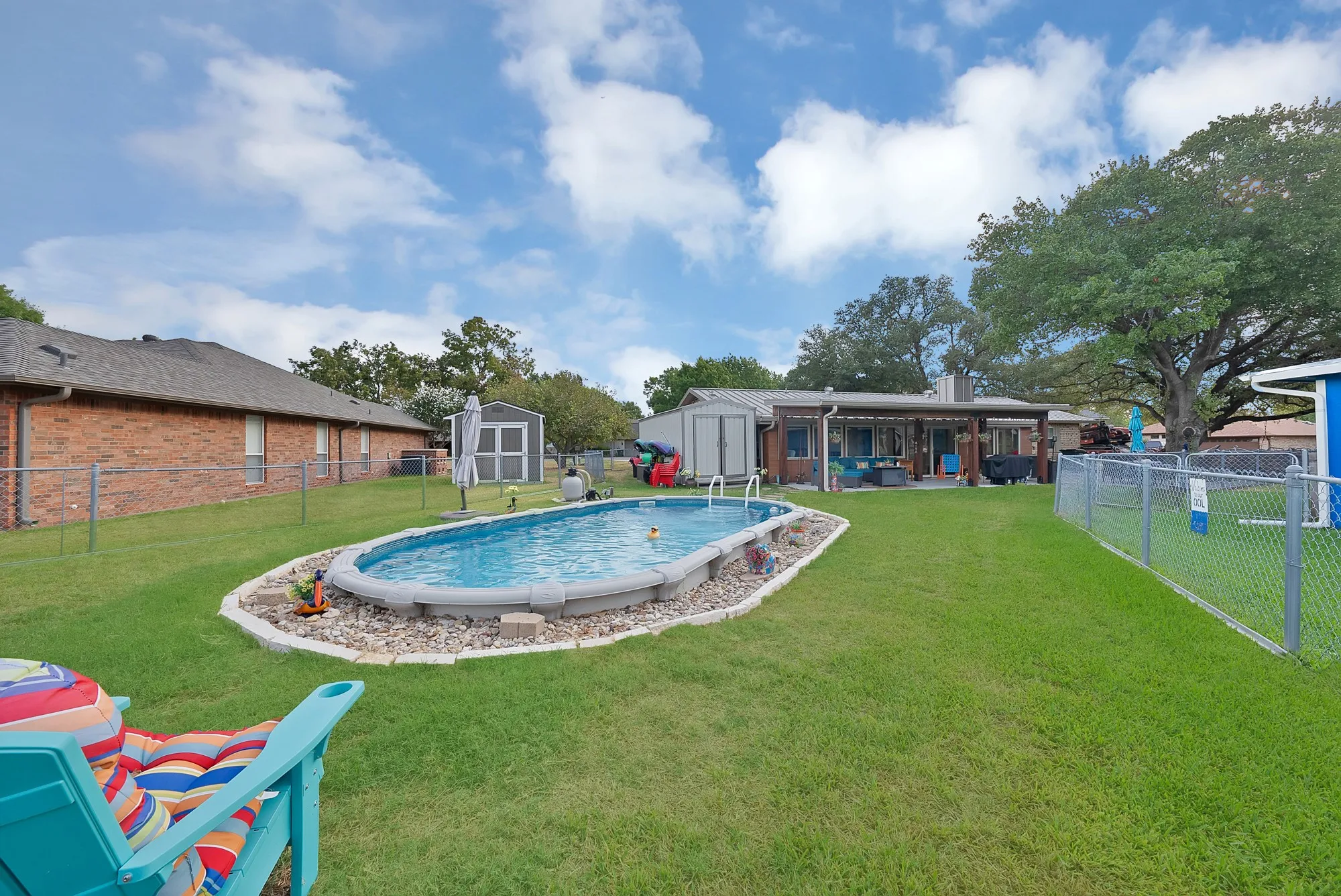 Expansive backyard featuring an above-ground pool with stone landscaping, a covered patio, and a storage shed