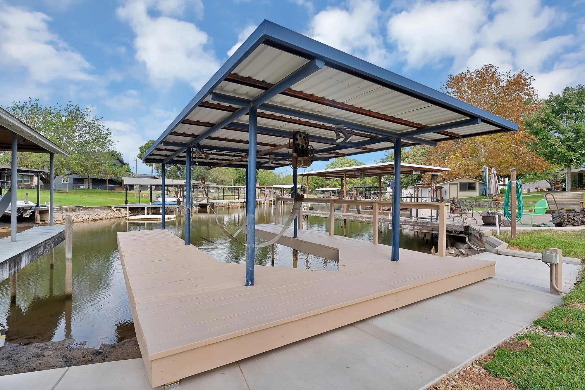 Covered boat dock featuring a boat lift, composite decking, and concrete pathway