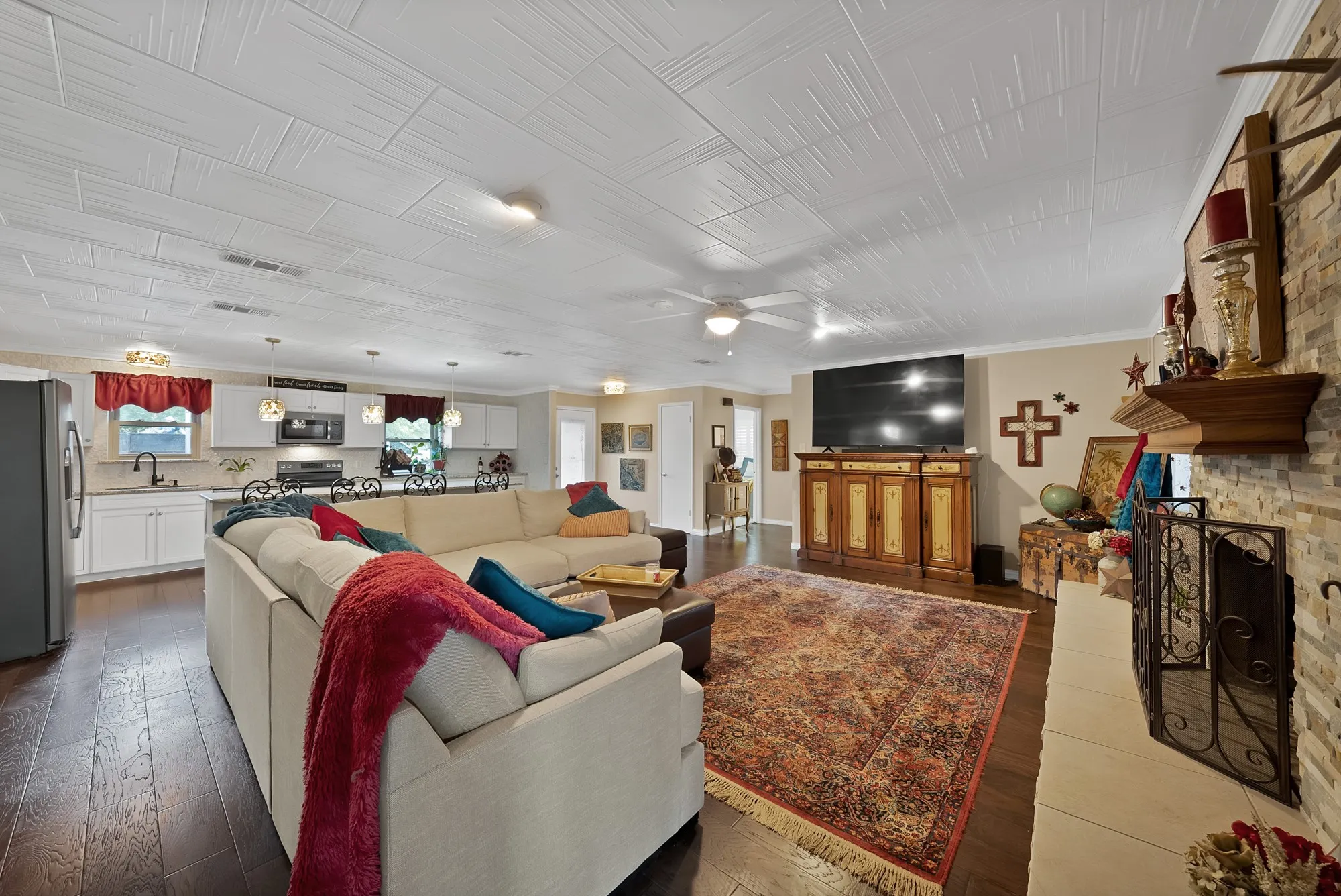 Open-concept living space featuring wood-finish flooring, a stone-clad fireplace with a decorative mantel, and a textured ceiling