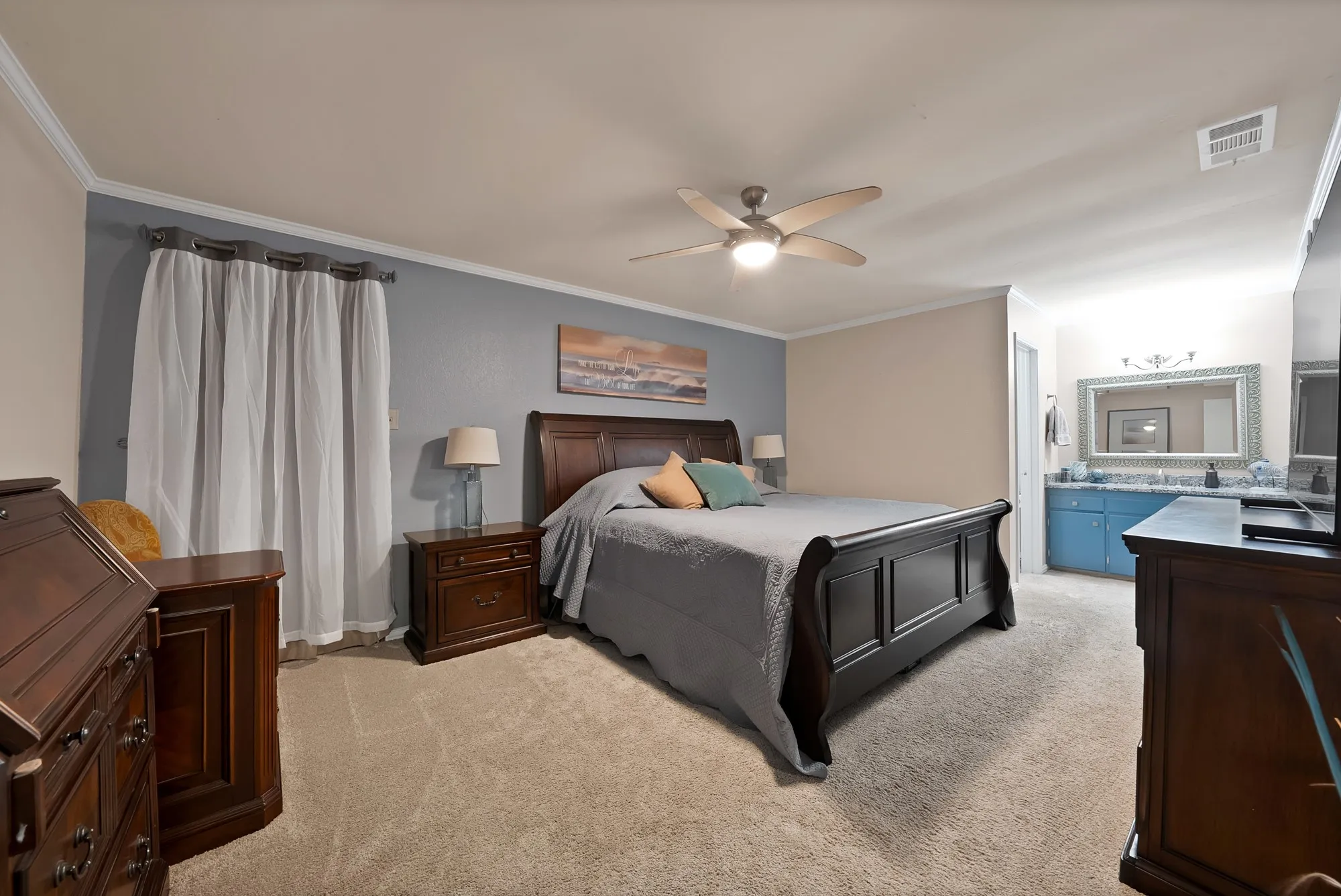 Plush carpet flooring, ceiling fan with integrated lighting, crown molding, and a built-in vanity with a countertop sink