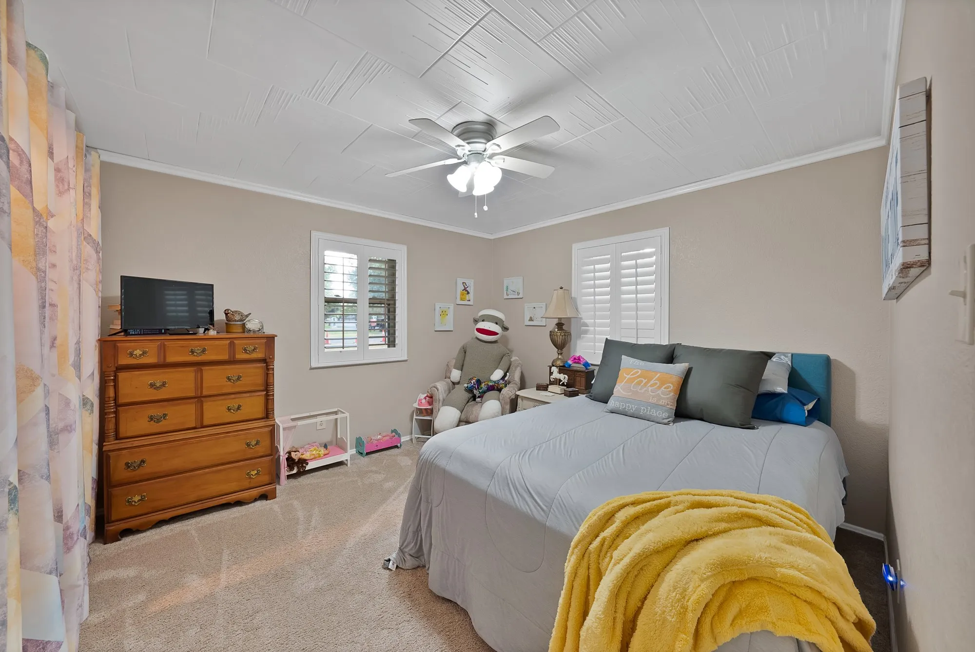 Textured ceiling with crown molding, ceiling fan, carpeted flooring, and white window shutters
