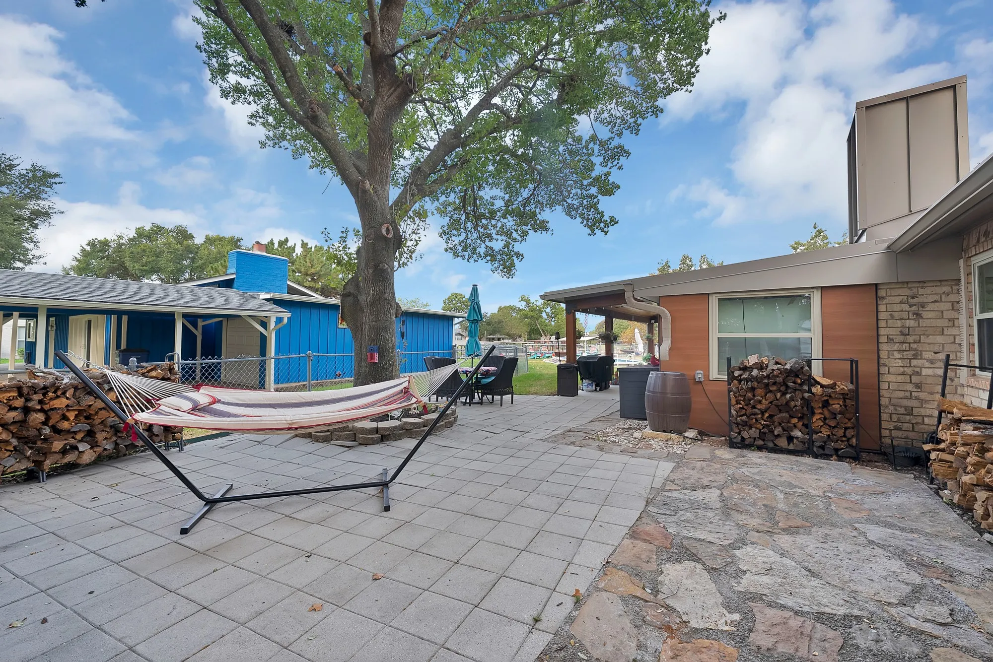Expansive patio featuring a mix of flagstone and paver surfaces, mature trees, a covered outdoor area, and brick exterior elements