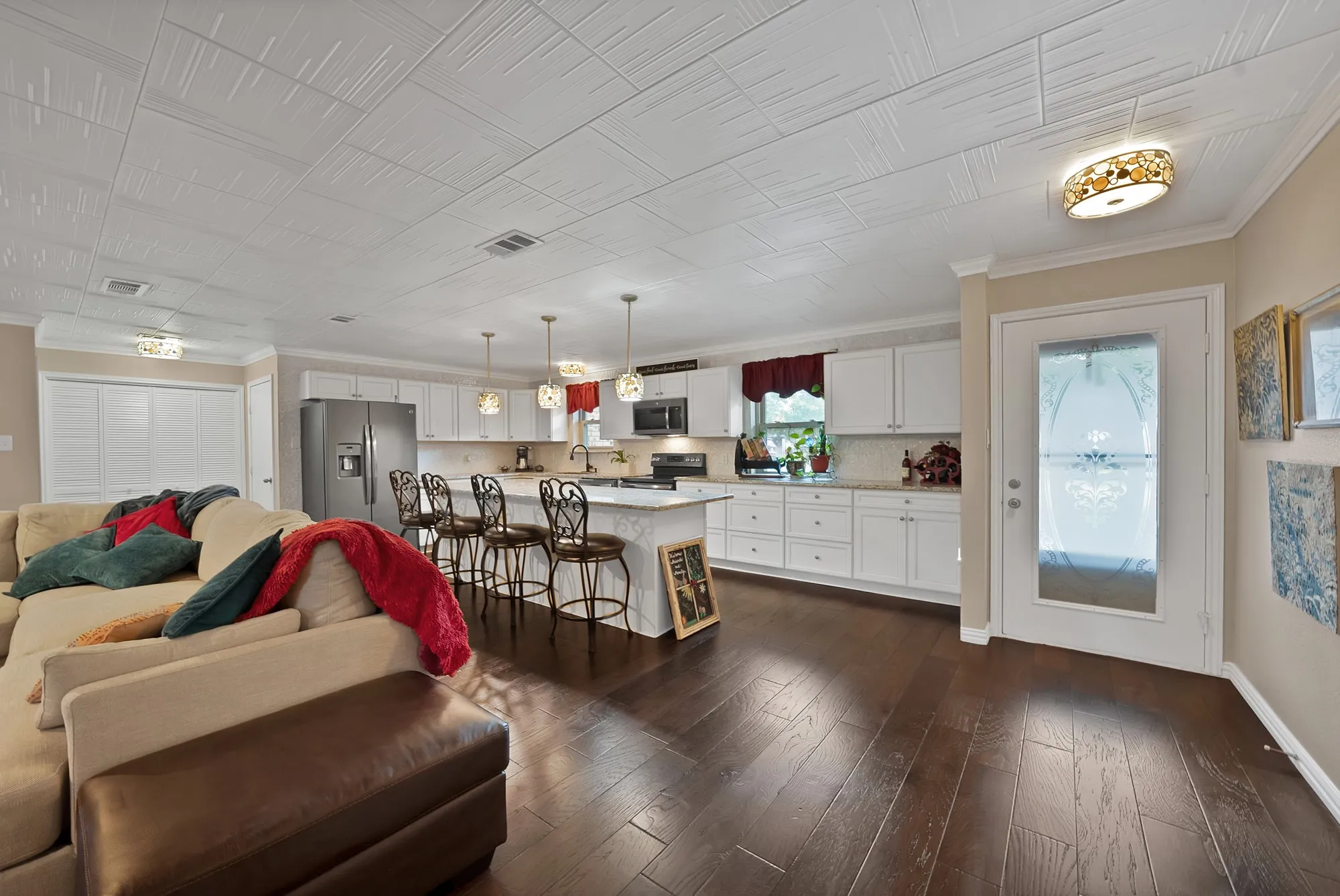 Dark wood-finish flooring, white cabinetry, island with seating, stainless steel appliances, and a glass-paned door