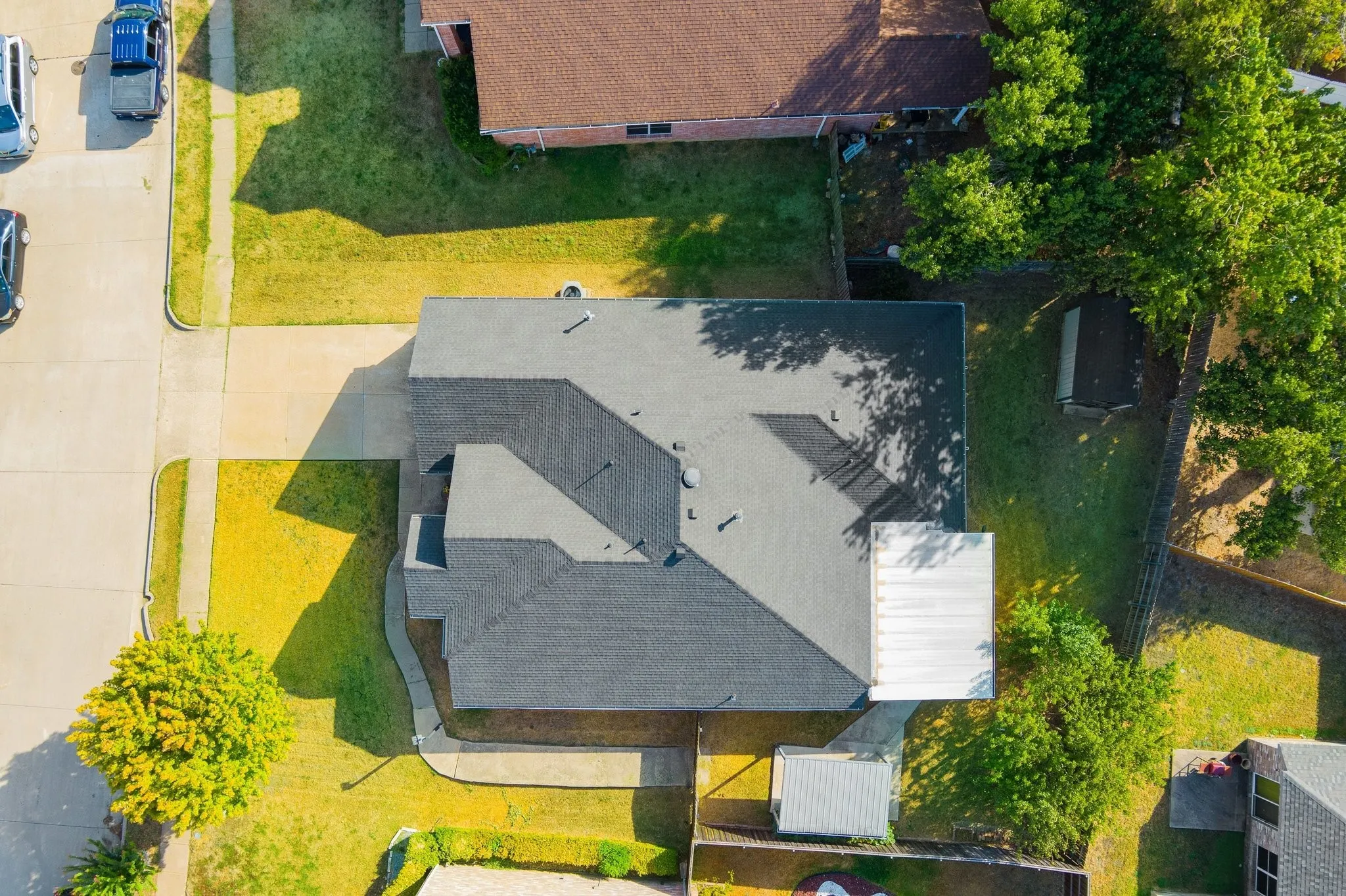 Expansive lot featuring a concrete driveway, established trees, and a gray shingled roof