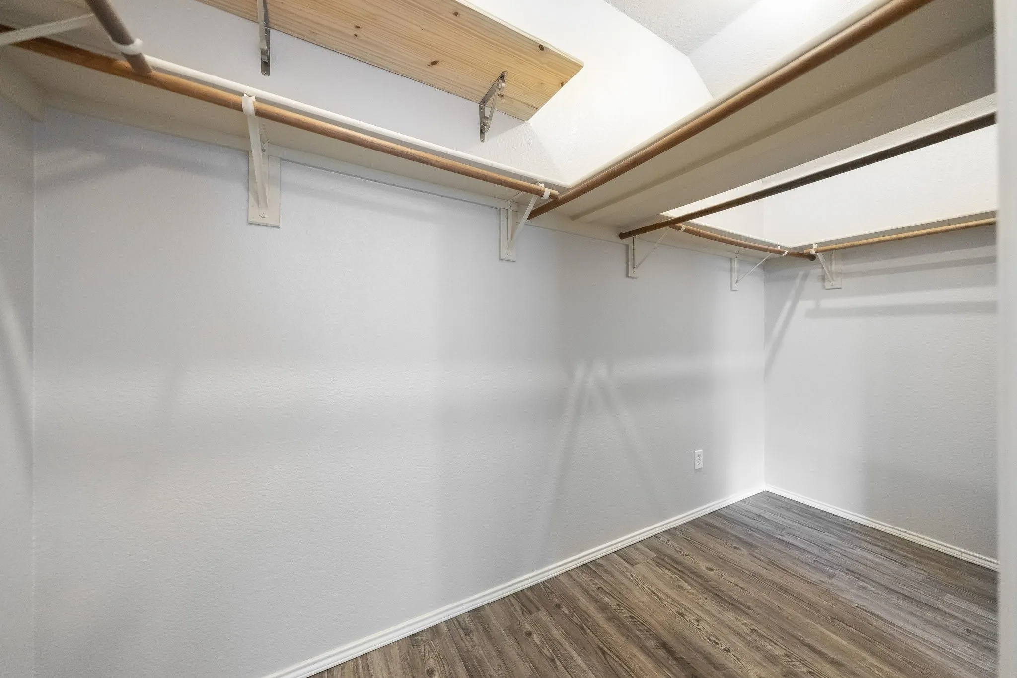 Walk-in closet featuring wood-finish flooring, white walls, and built-in shelving with hanging rods