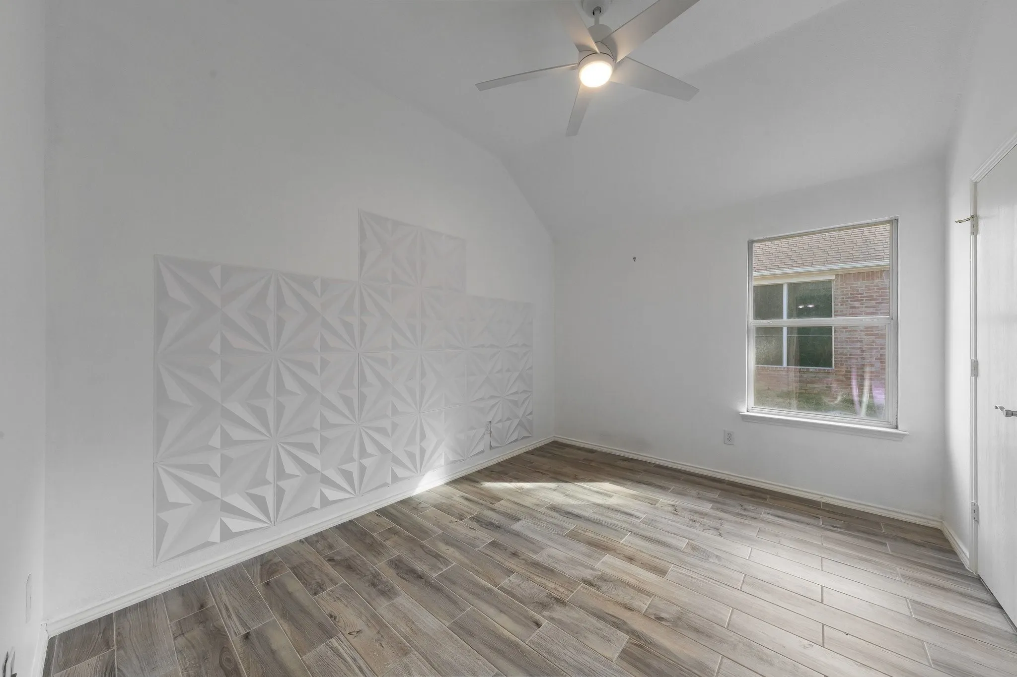 Vaulted ceiling, wood-finish flooring, ceiling fan with integrated lighting, window, and textured wall panels