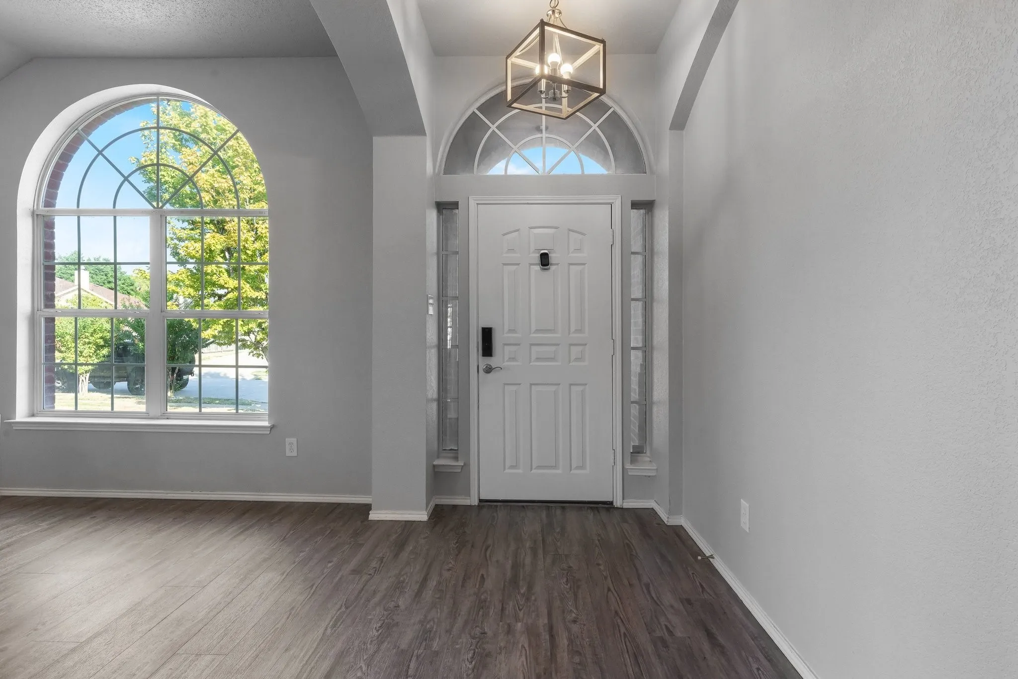 Arched transom window above the entry door with sidelights, wood-finish flooring, and an arched window