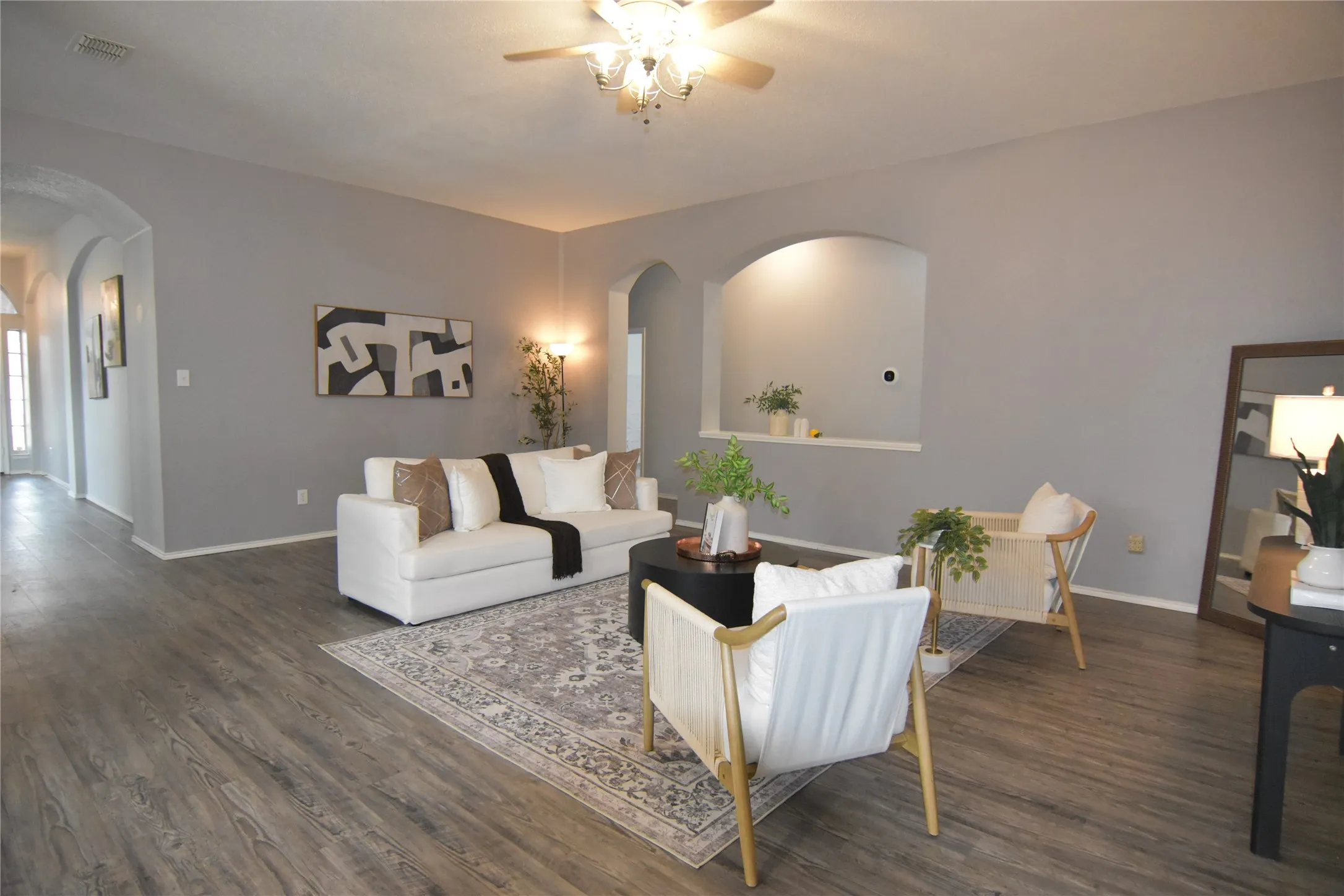 Wood-finish flooring, recessed wall niche, arched doorways, light gray walls, and a ceiling fan with integrated lighting
