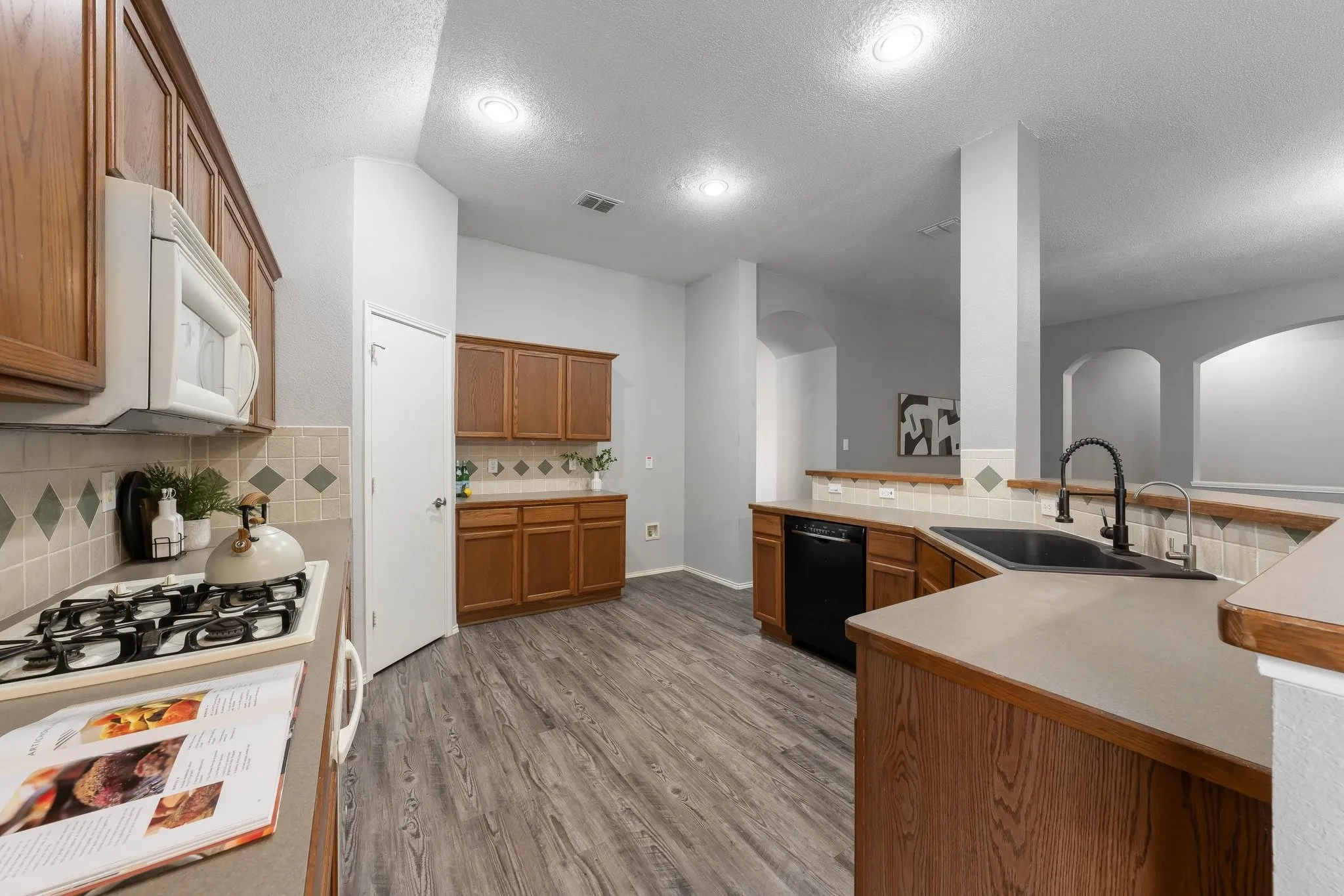 Kitchen featuring extensive wood cabinetry, wood-finish flooring, a black sink with a matte black faucet, and a gas range