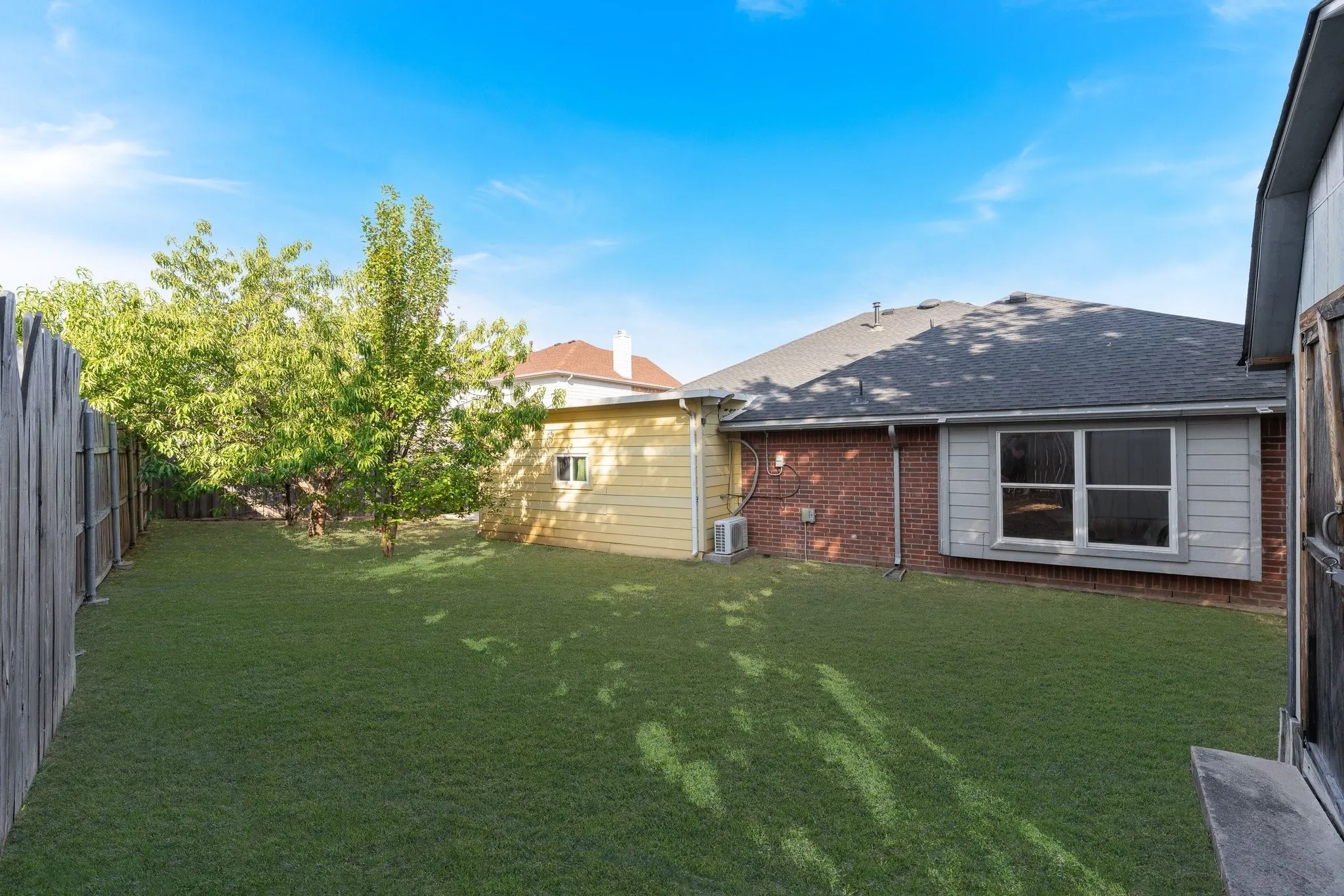Expansive backyard featuring a manicured lawn, mature trees, and a wooden privacy fence