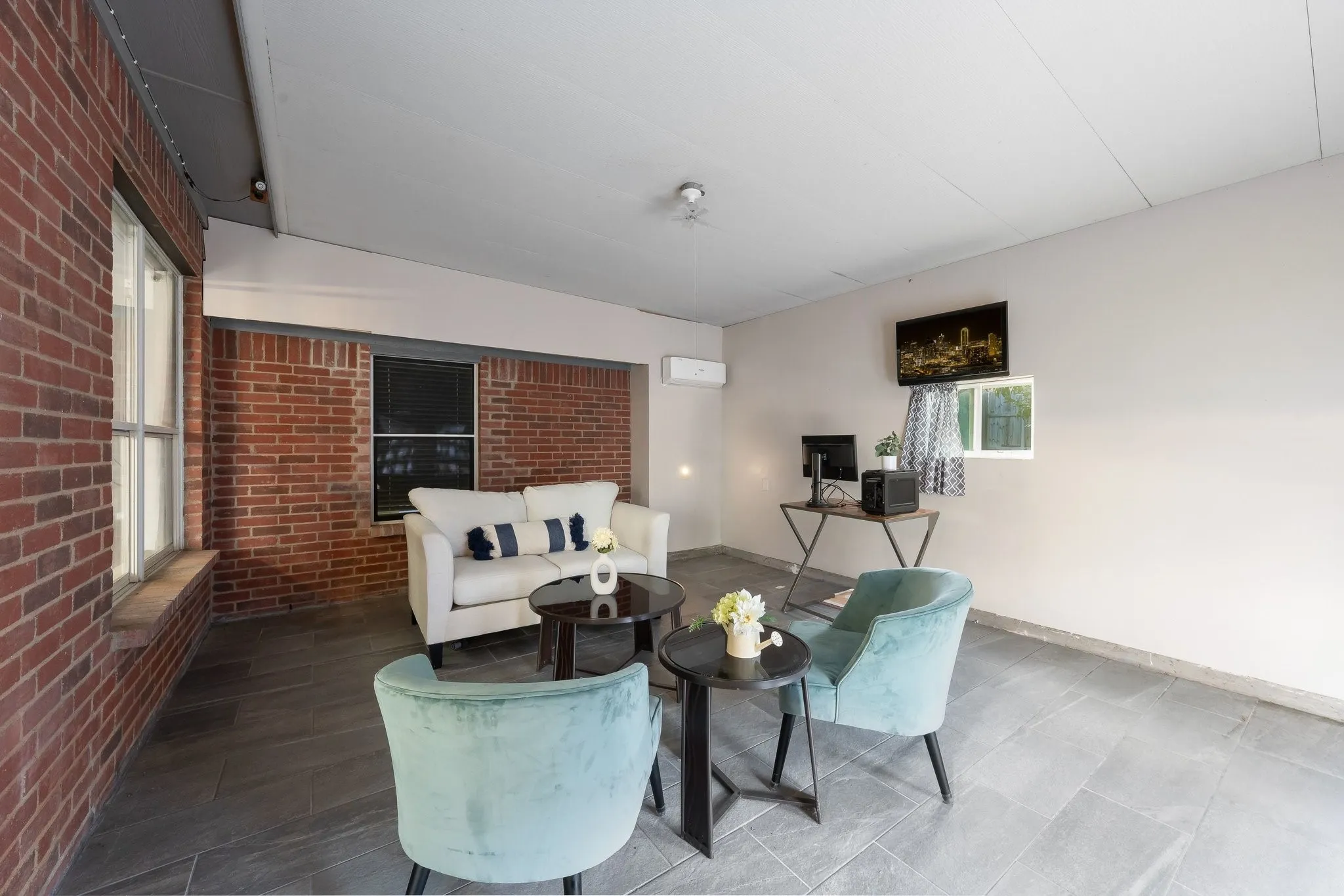 Brick wall accent, grey tile flooring, window with blinds, ceiling-mounted light fixture, wall-mounted air conditioning unit