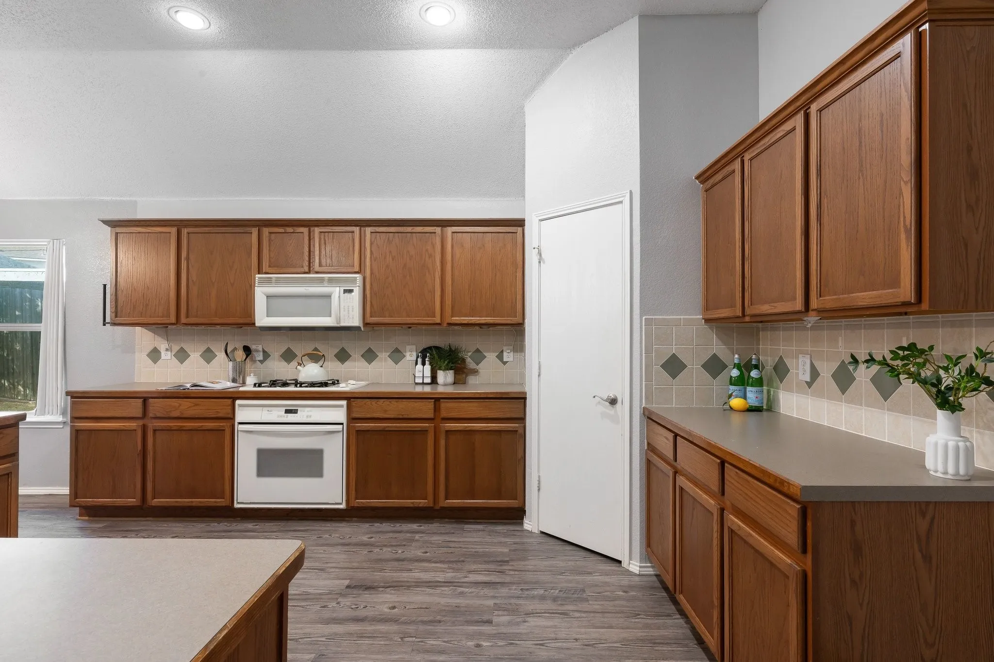 Kitchen featuring wood cabinetry, light countertops, integrated white appliances, and wood-finish flooring