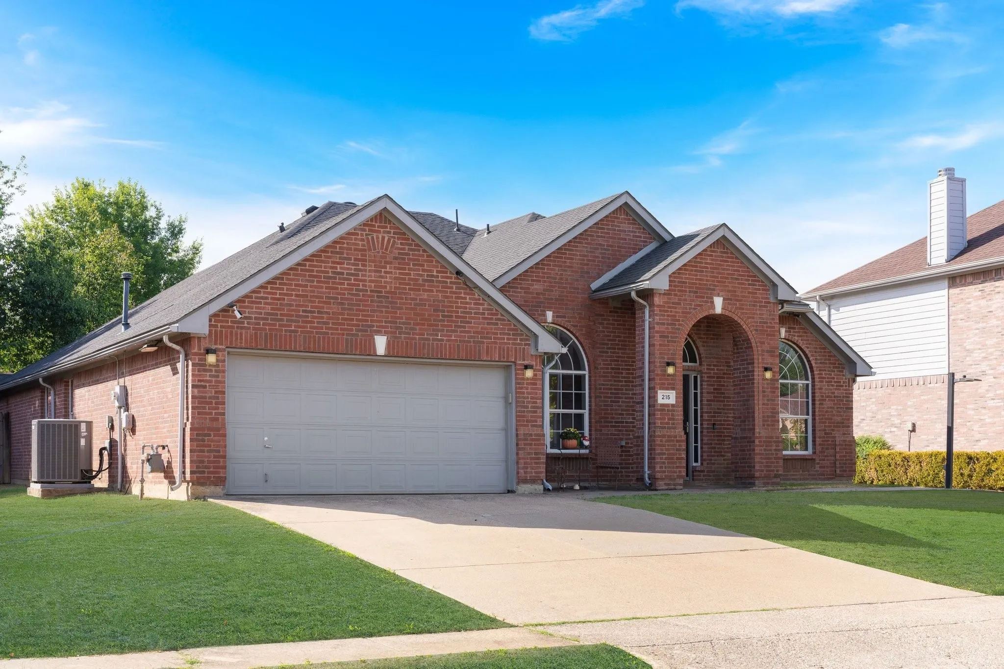 Brick exterior with arched entry and windows, attached garage, and concrete driveway
