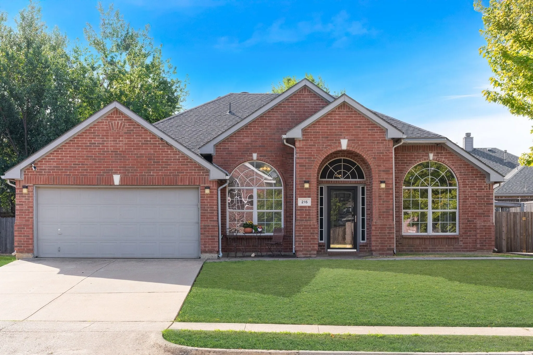 Red brick exterior featuring a dark composition shingle roof, arched transom windows, and an attached two-car garage