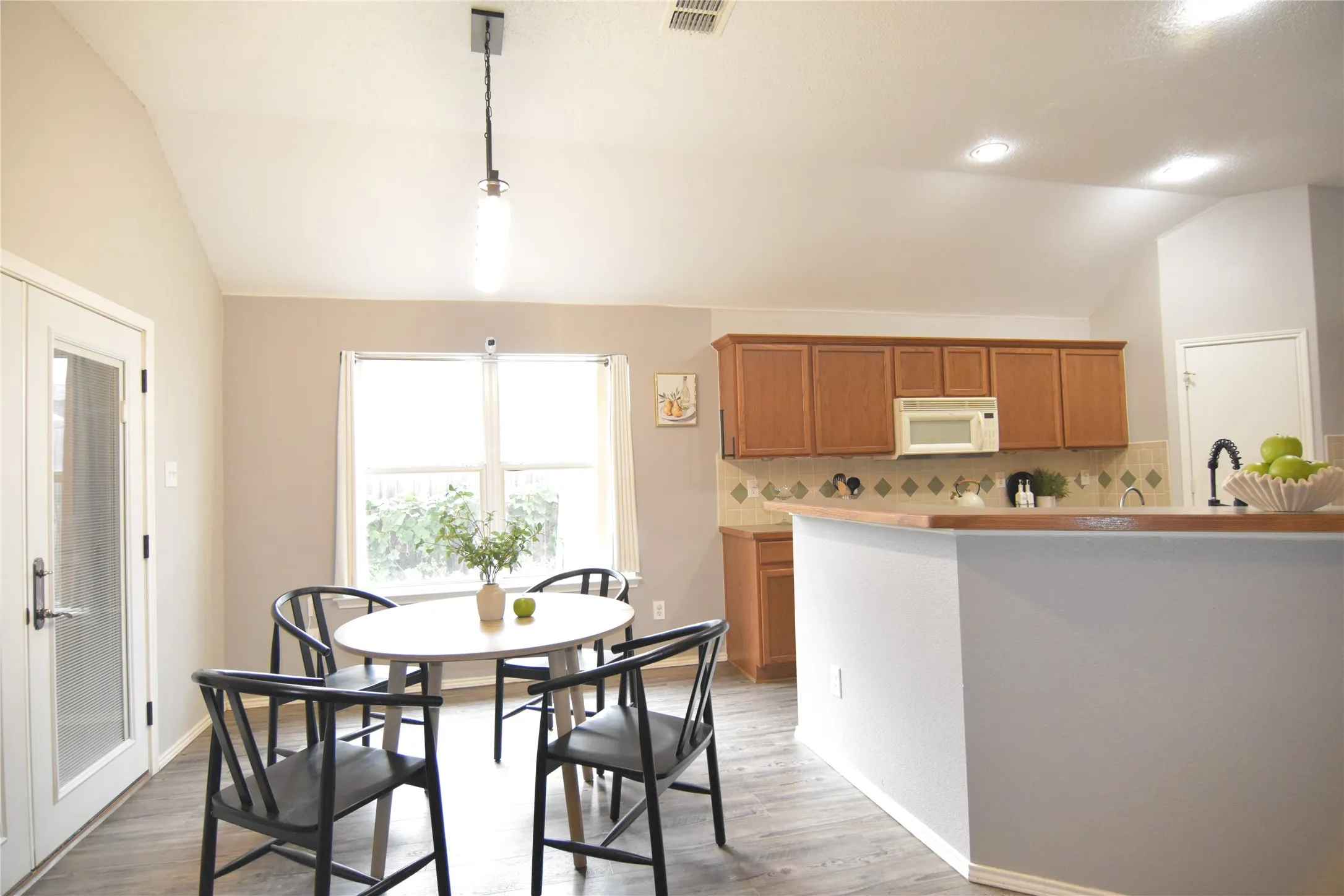 Vaulted ceiling with recessed lighting, wood-finish flooring, kitchen with wood cabinetry, tiled backsplash, and a window for natural illumination