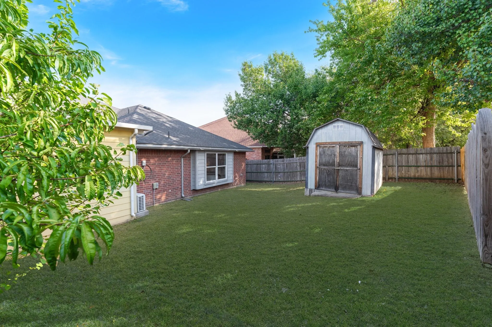 Expansive grassy yard with a privacy fence, an outbuilding, and mature trees