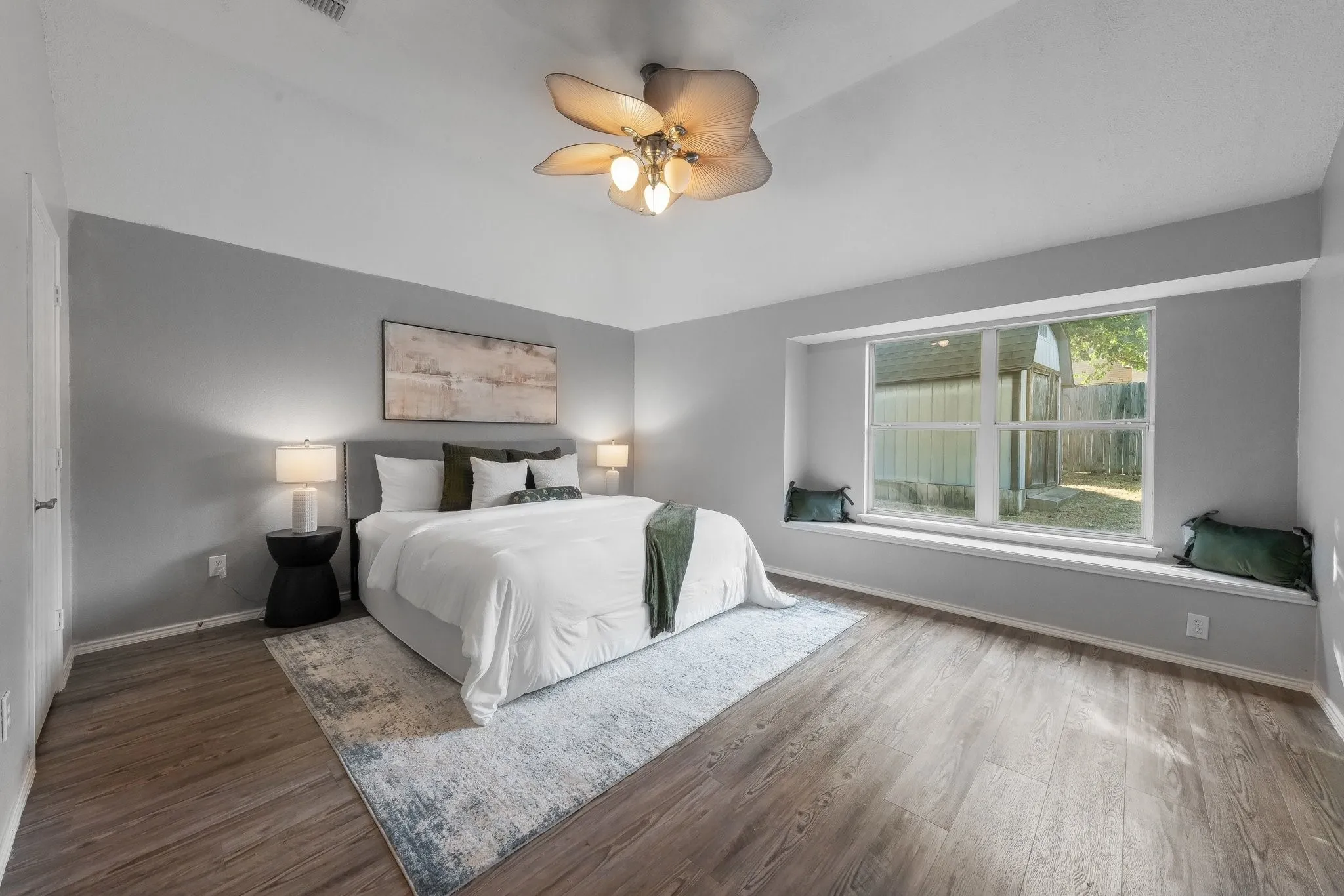 Spacious primary bedroom featuring wood-finish flooring, soft gray walls, and abundant natural light from large multi-pane windows