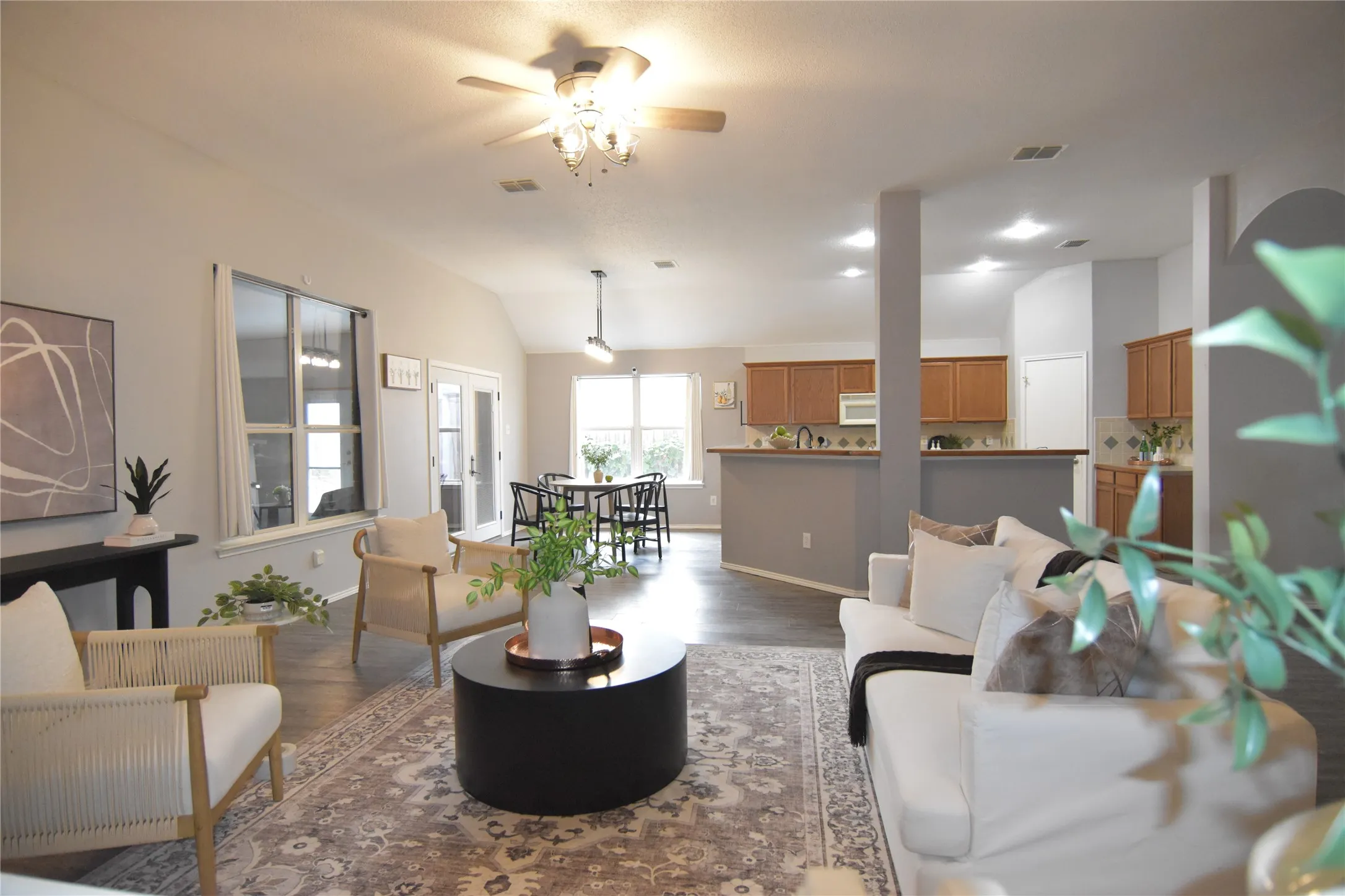 Vaulted ceiling with a ceiling fan, wood-finish flooring, recessed lighting, double French doors, and an open-concept kitchen with light wood cabinetry