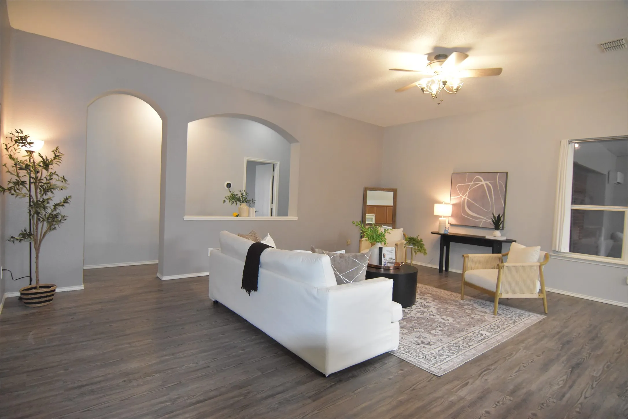 Recessed archways, wood-finish flooring, ceiling fan with integrated lighting, window with white trim, and light gray wall paint