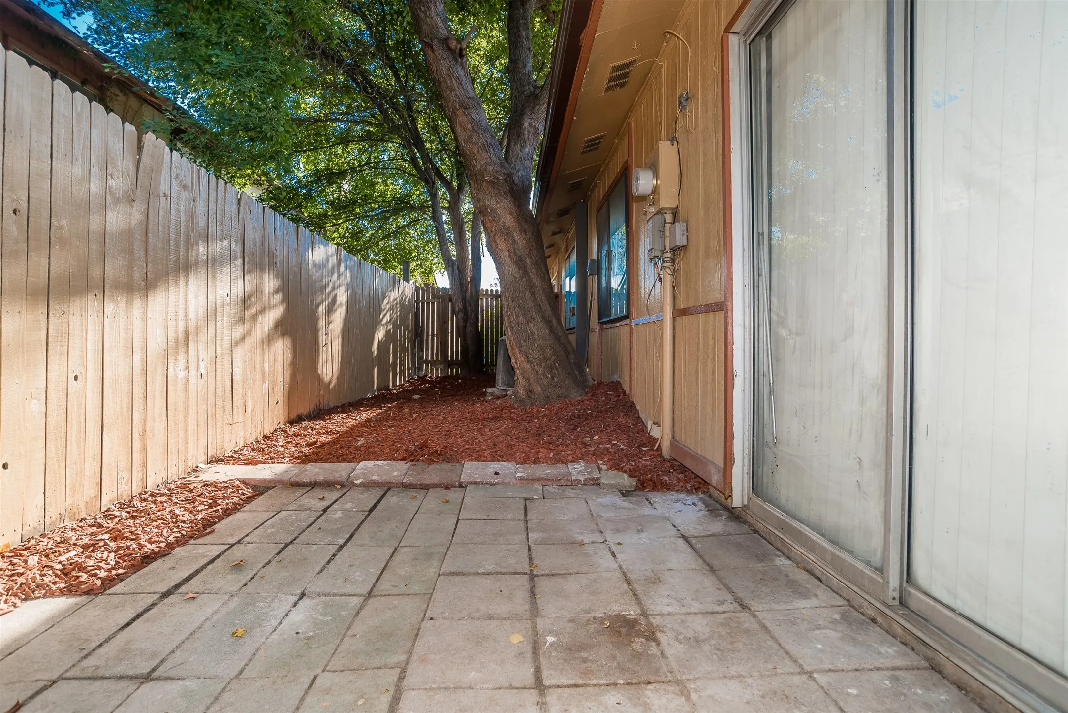 Paved patio area with a privacy fence, mature trees, and landscaping