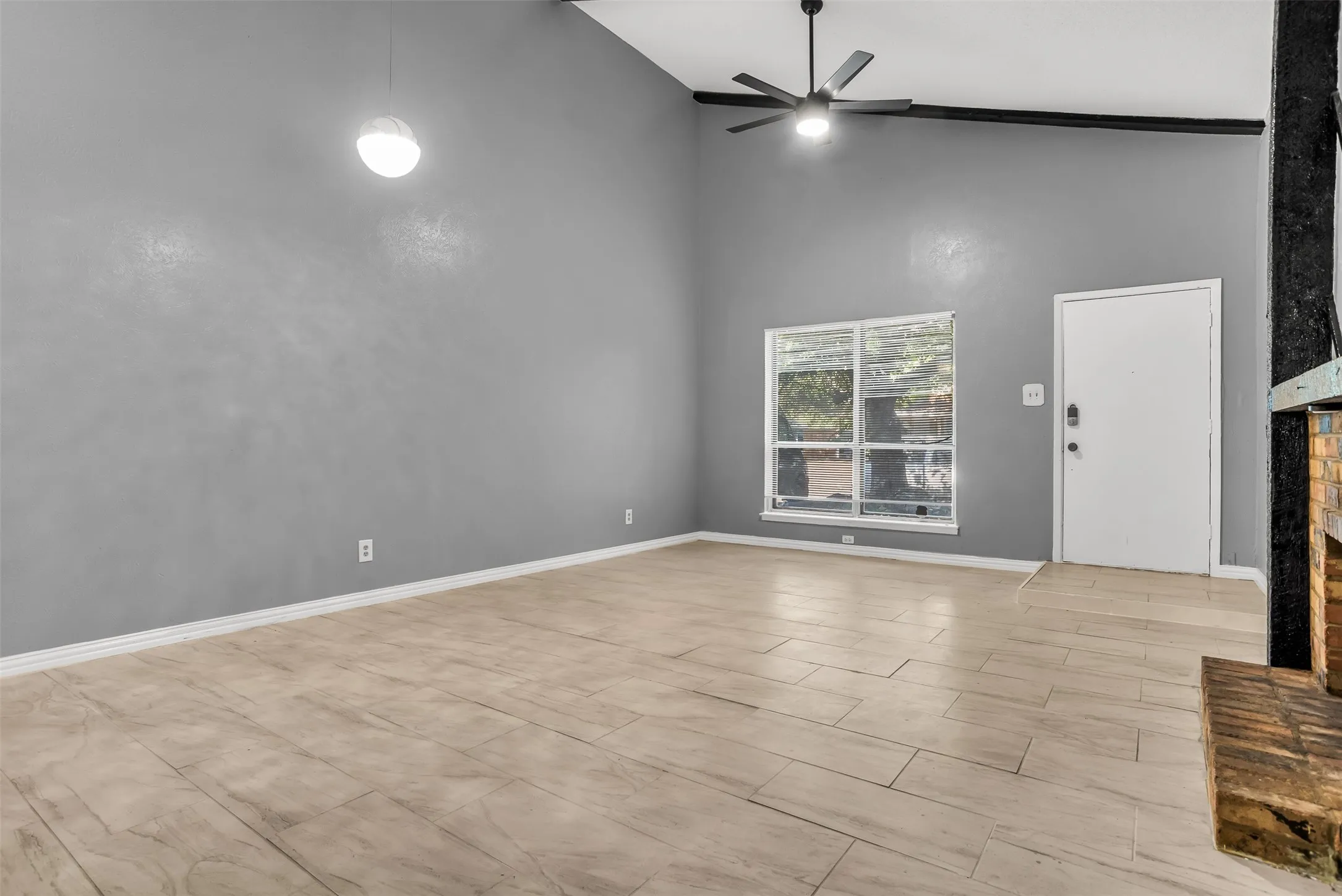 Vaulted ceiling with exposed beam, wood-finish flooring, ceiling fan, and a brick-finish fireplace