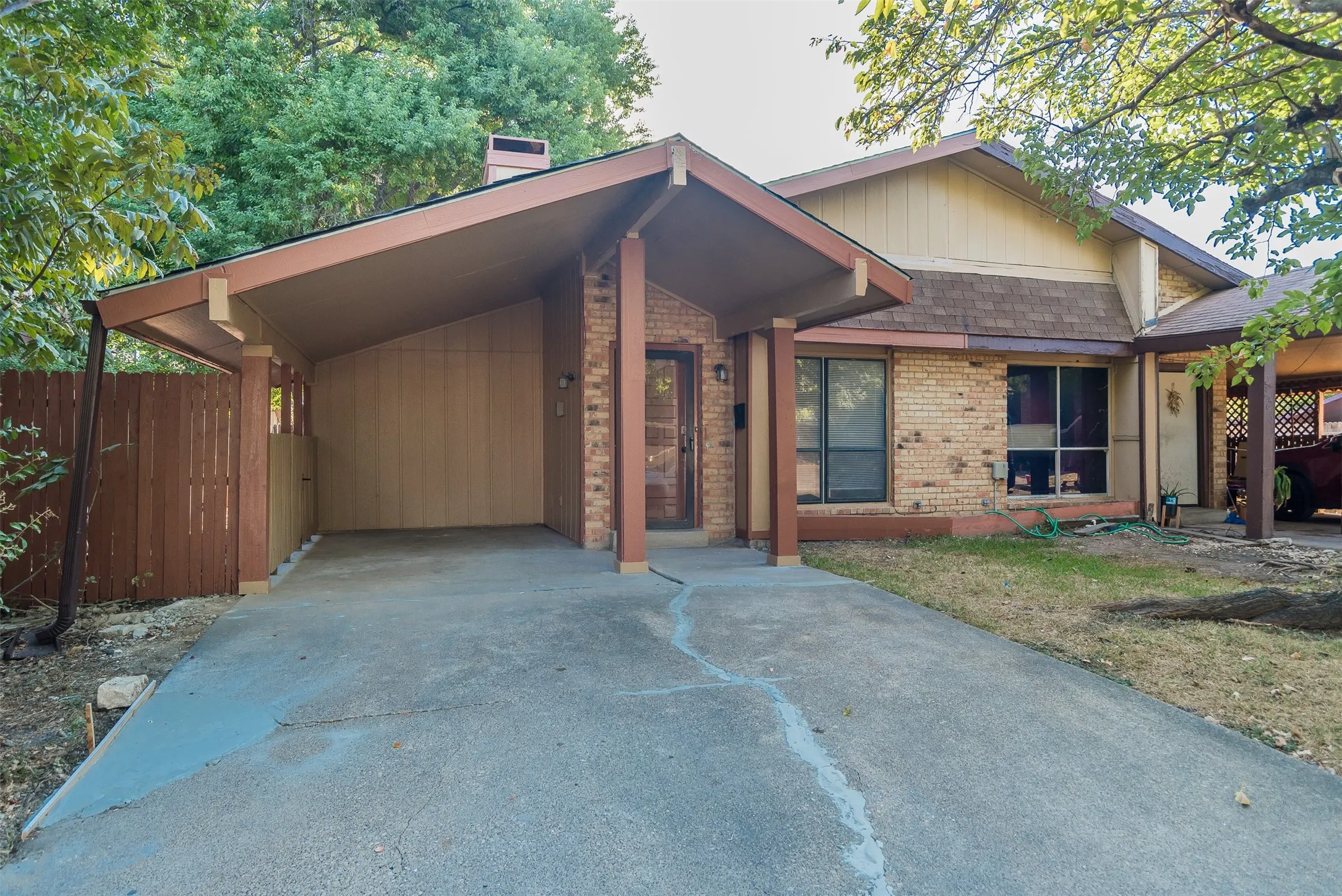 Brick exterior featuring a covered carport, pitched roofline, and mature trees
