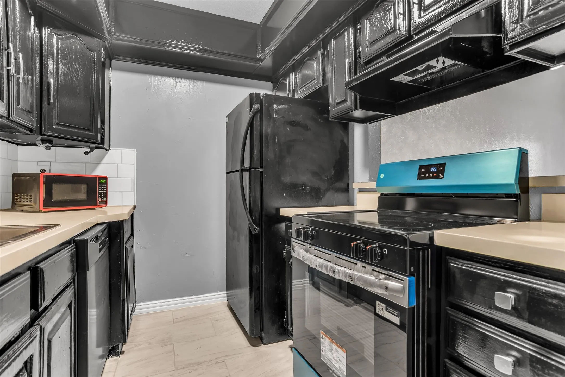 Galley kitchen featuring black cabinetry, light-toned countertops, a white subway tile backsplash, and light-colored tile flooring