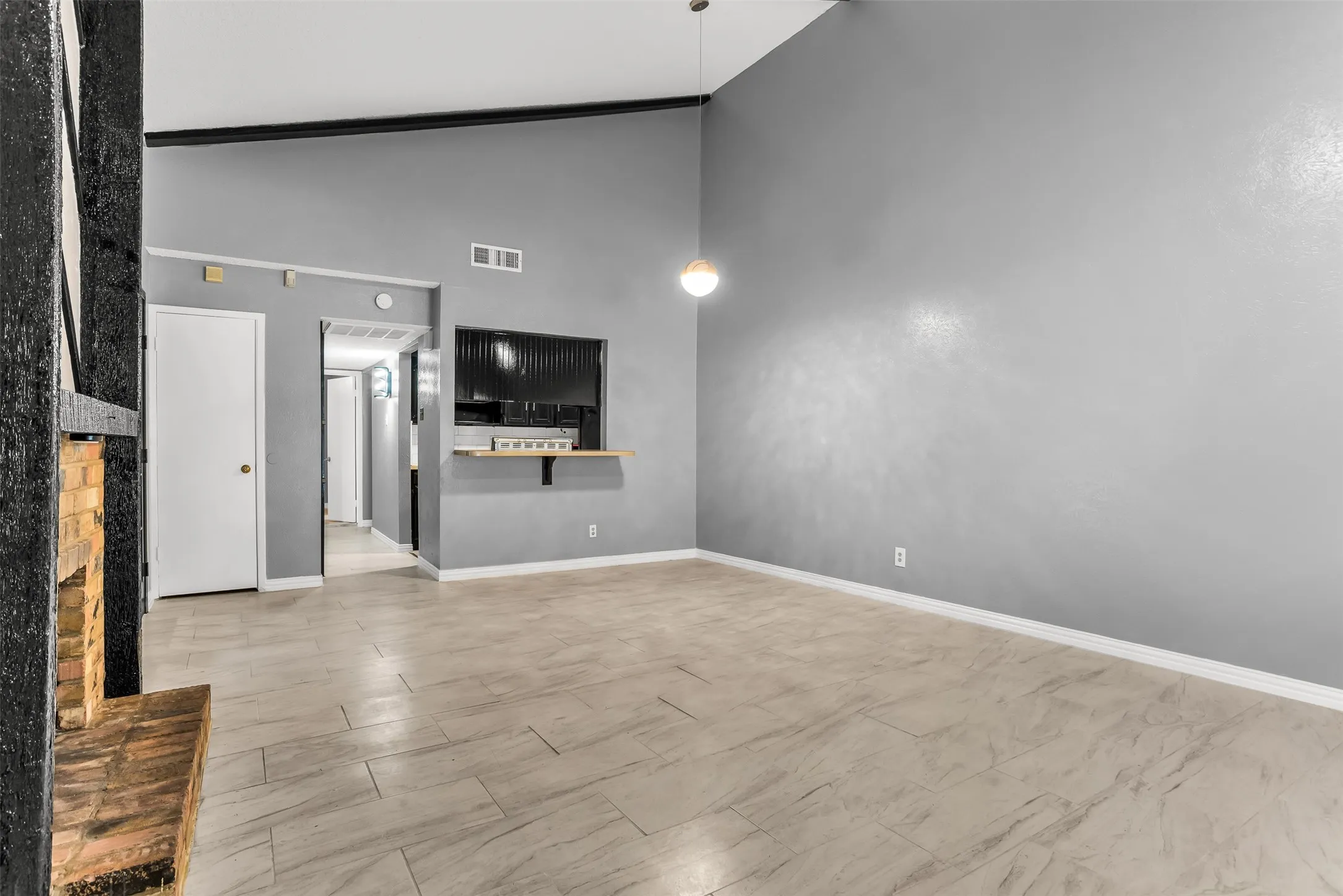 Vaulted ceilings, tile flooring, brick fireplace, pass-through window with wood ledge, and an attached pendant light fixture