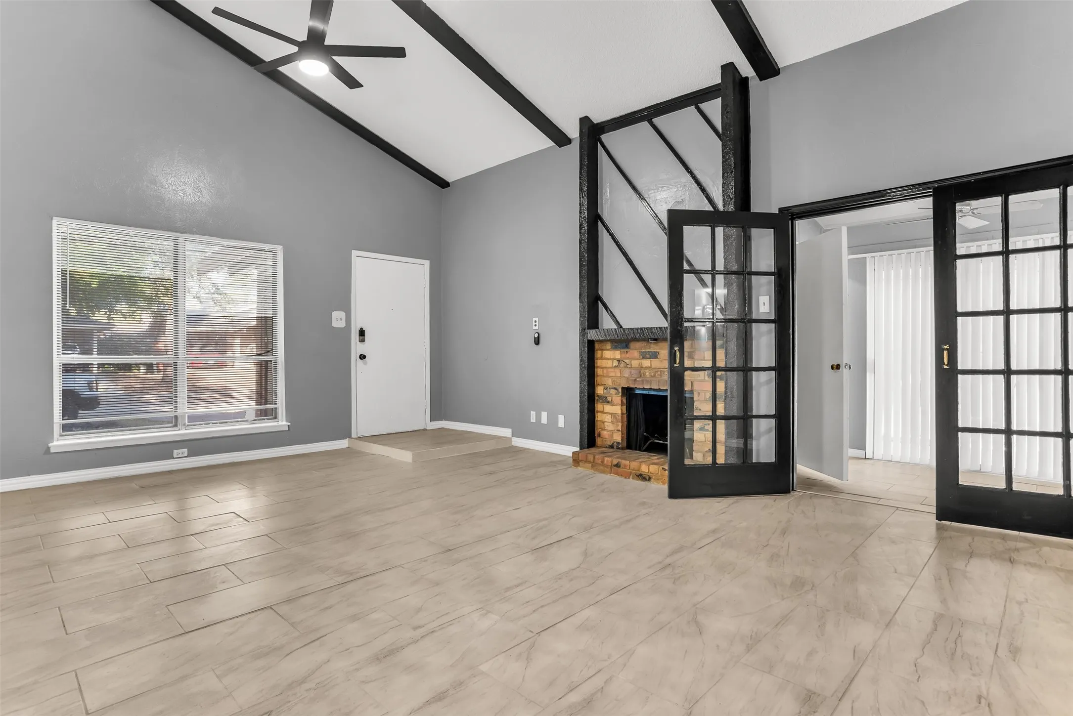 Vaulted ceiling with exposed beams, brick fireplace, wood-finish flooring, and French doors