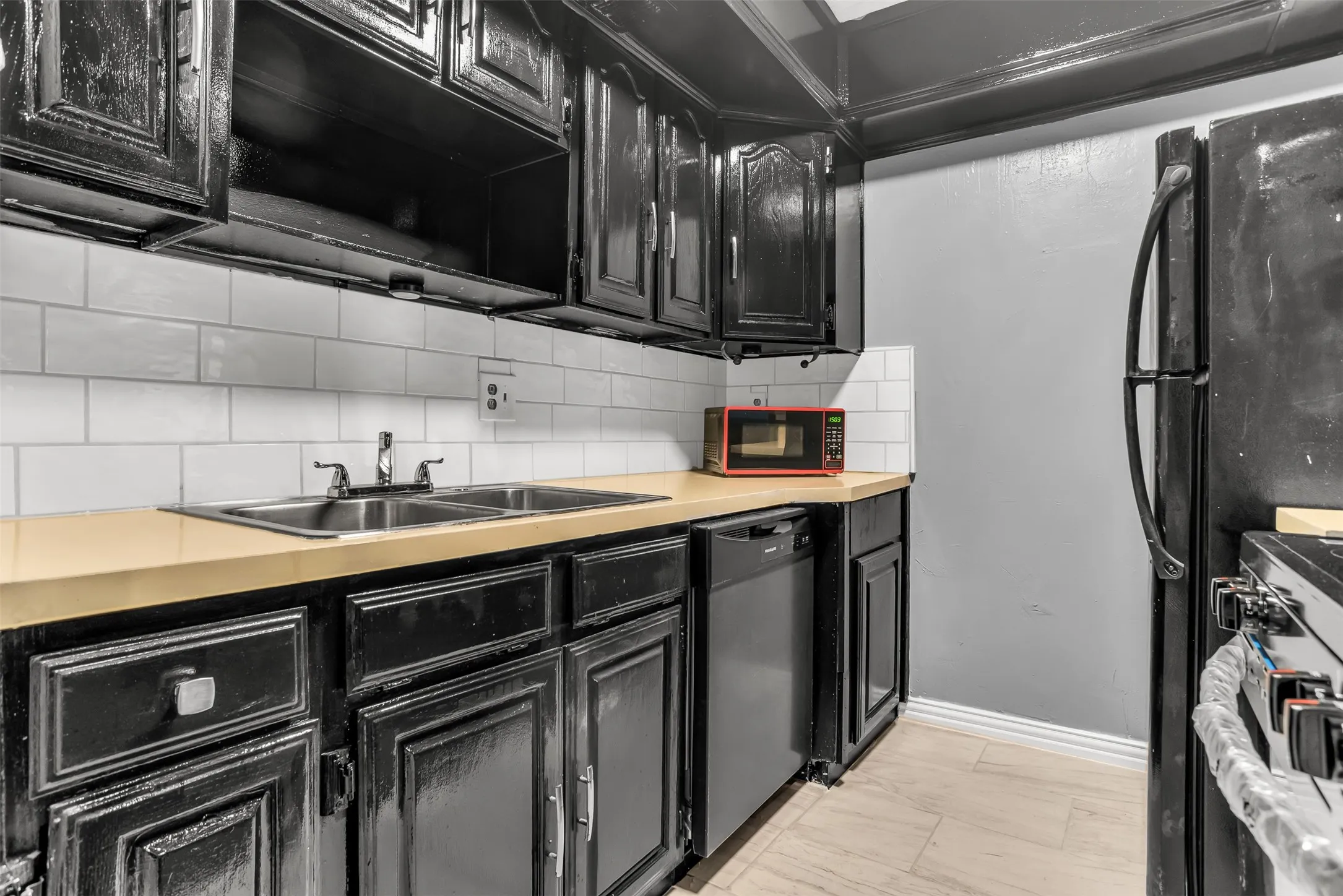 Kitchen featuring black cabinetry, light-toned countertops, a stainless steel double basin sink, and a white subway tile backsplash