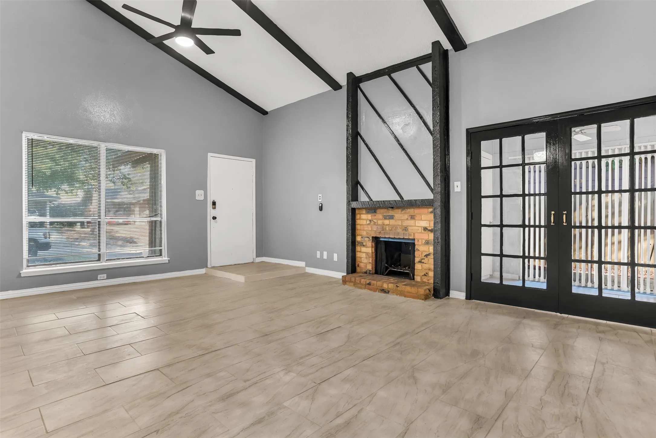 Vaulted ceiling with exposed beams, brick fireplace, wood-finish flooring, and black French doors