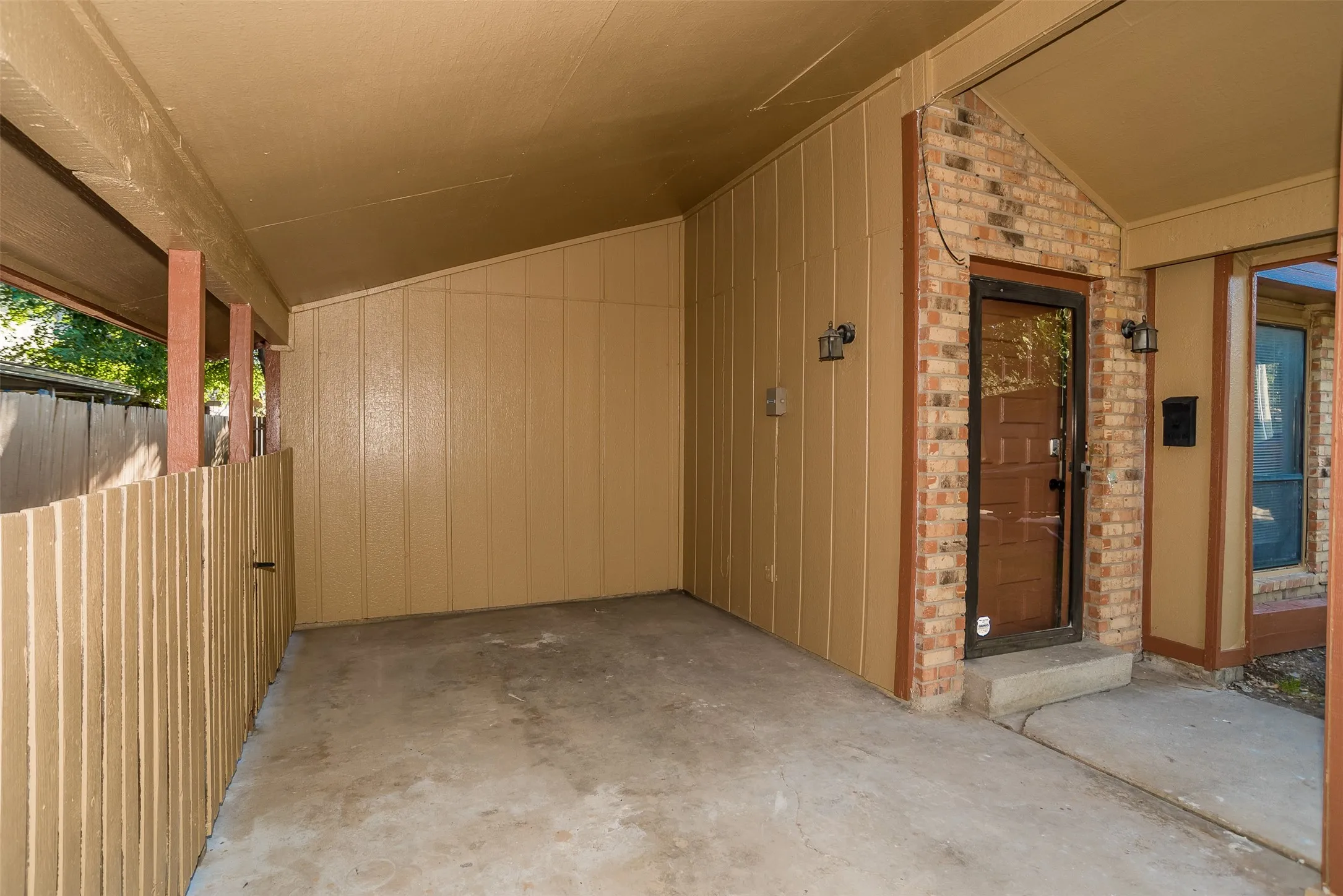 Covered entry with concrete flooring, brick facade, and wood-finish siding