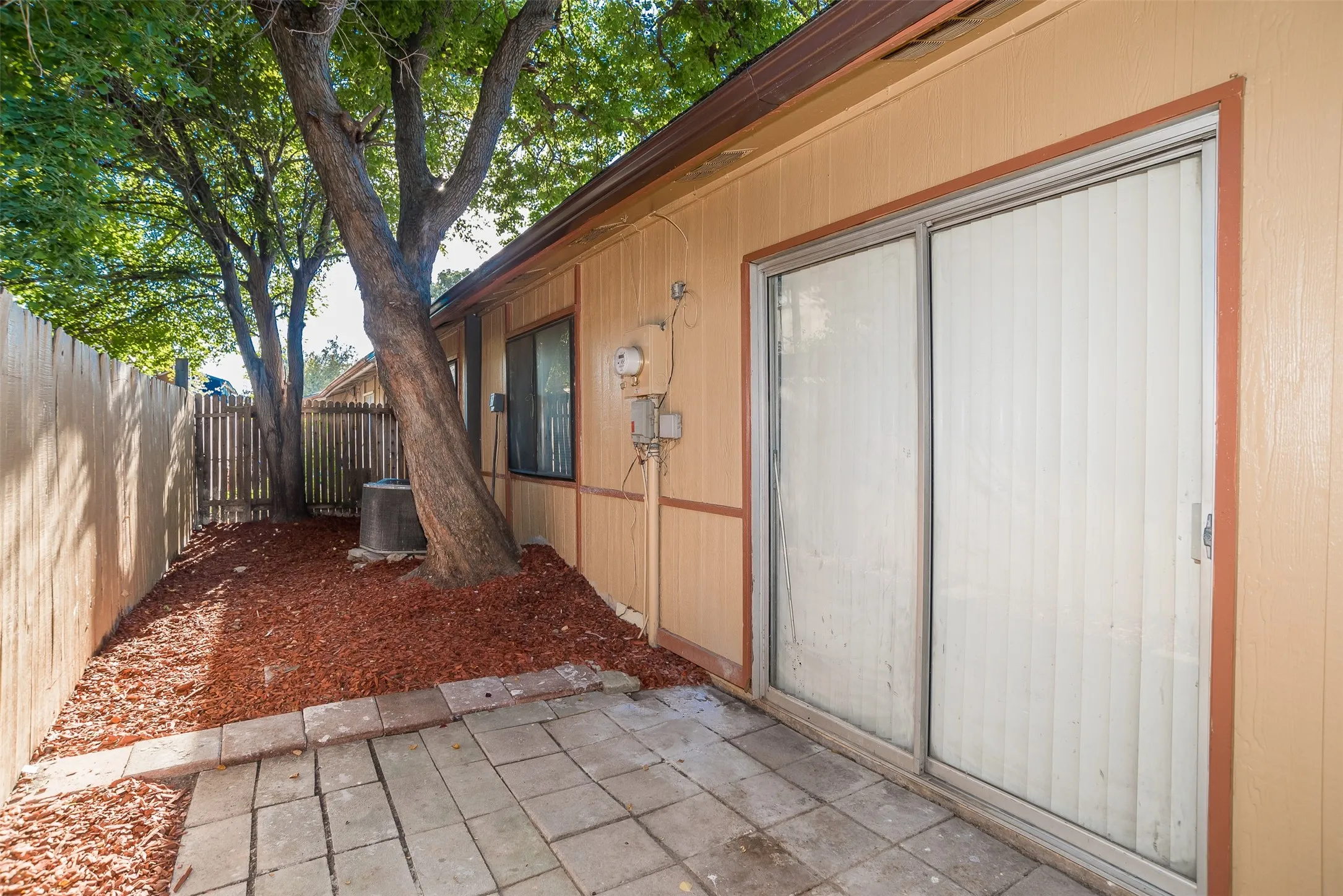 Private patio area featuring a paver stone surface, surrounded by rich brown mulch and mature trees