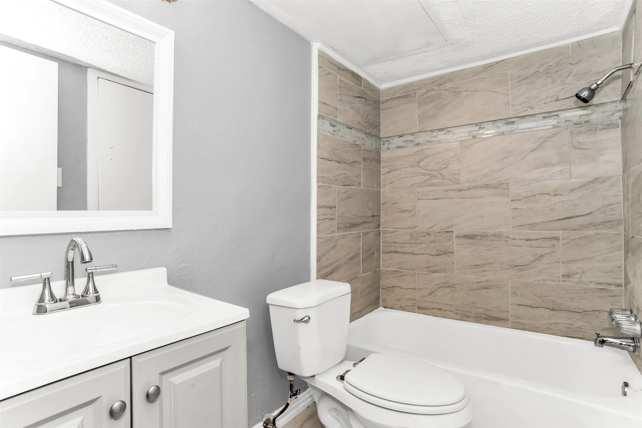Vanity with integrated sink, chrome faucet, white framed mirror, and tiled shower surround with accent strip